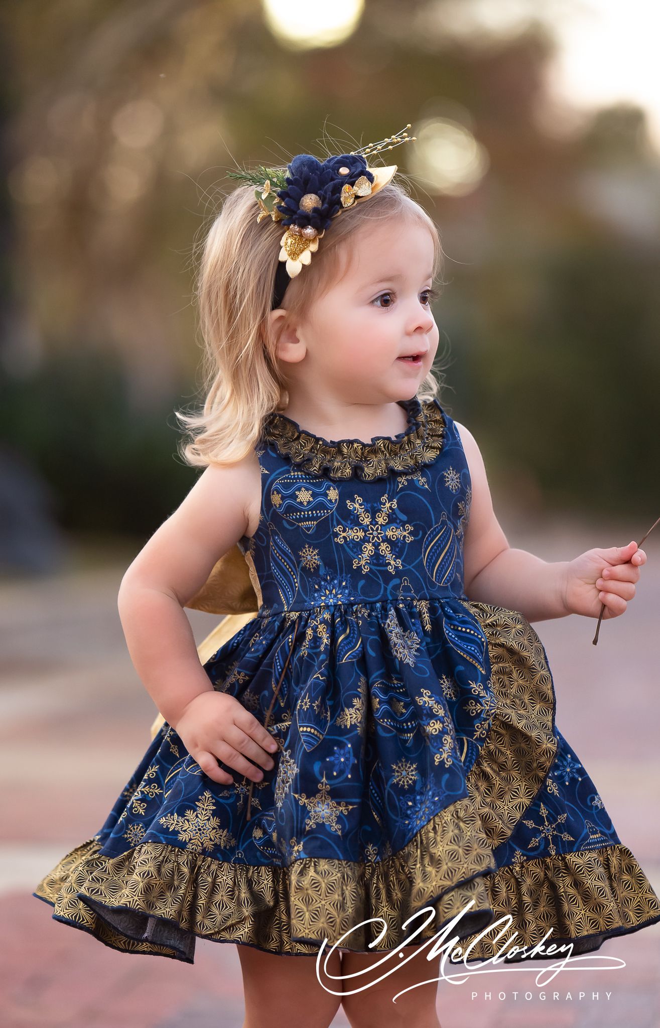 A small child wearing a navy blue and gold formal dress twirls and plays outdoors at dusk.