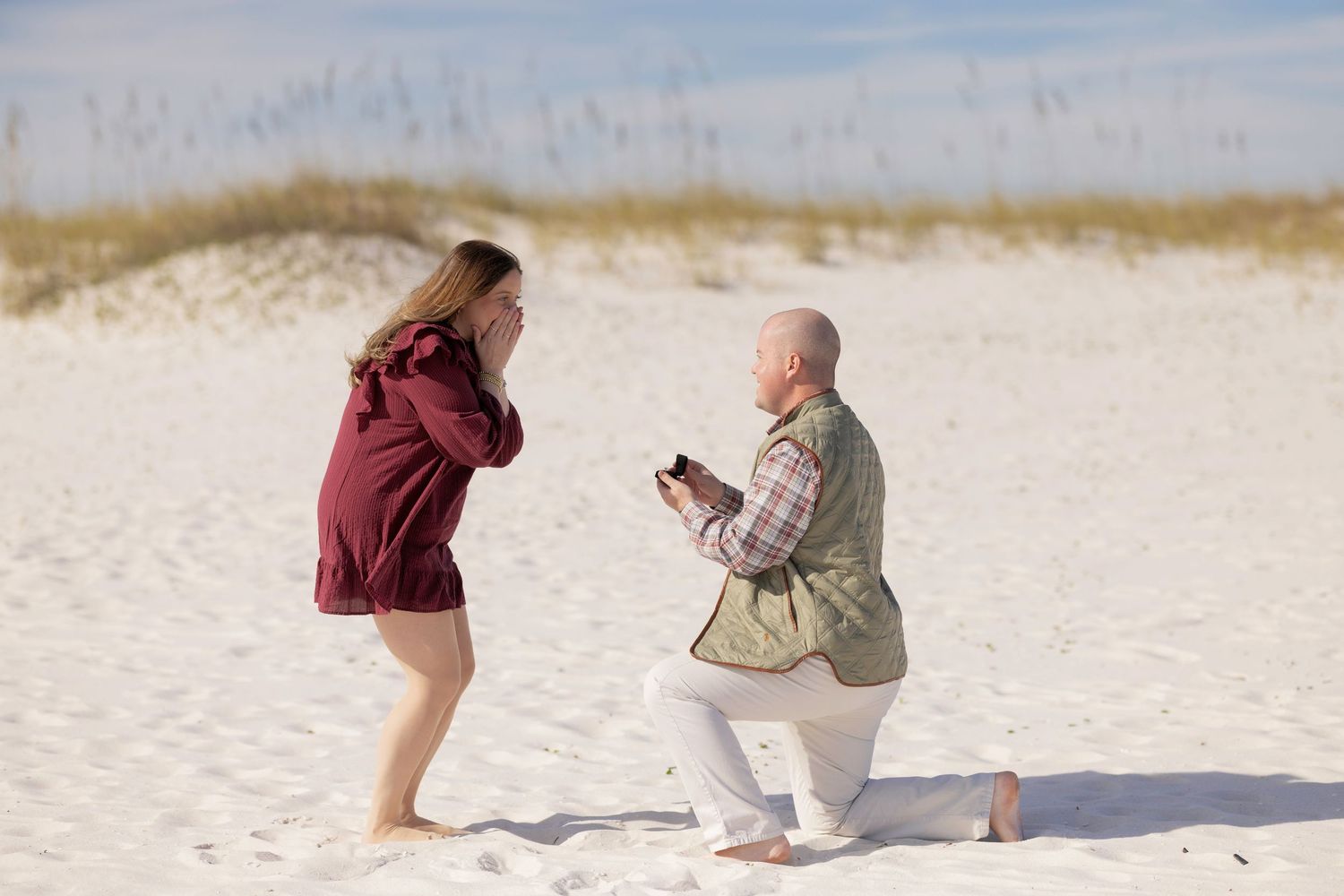 A romantic beach proposal scene with someone kneeling in the sand during sunset by the ocean.