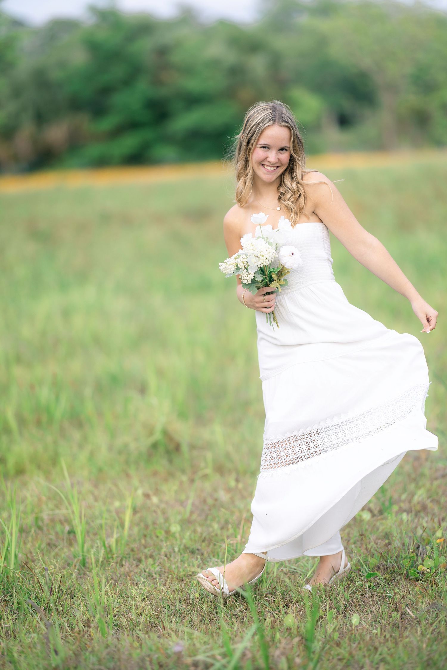 Woman in white dress twirls playfully in a green meadow during a summer photoshoot.