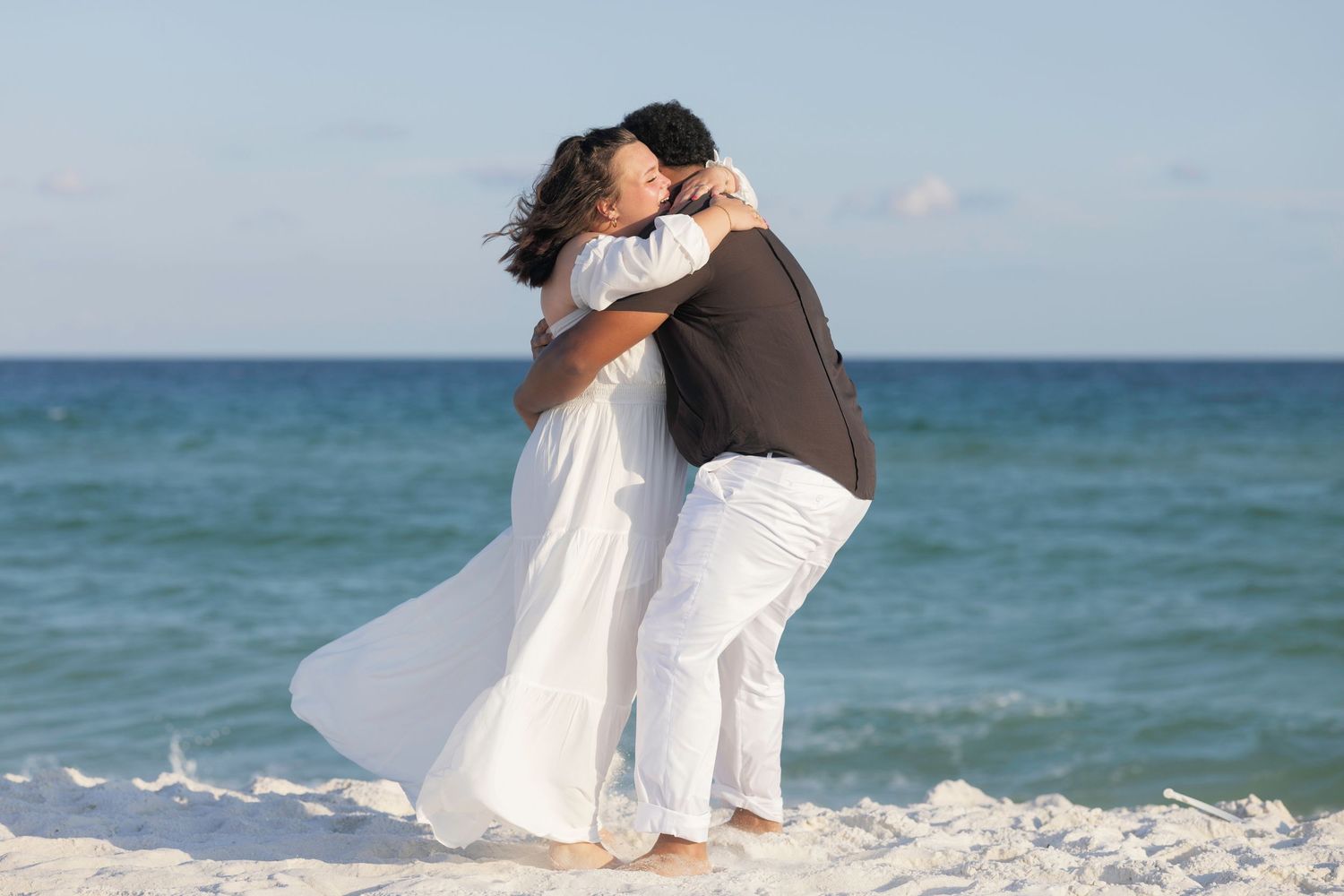 Couple embracing romantically on a white sand beach with turquoise ocean waves in the background.