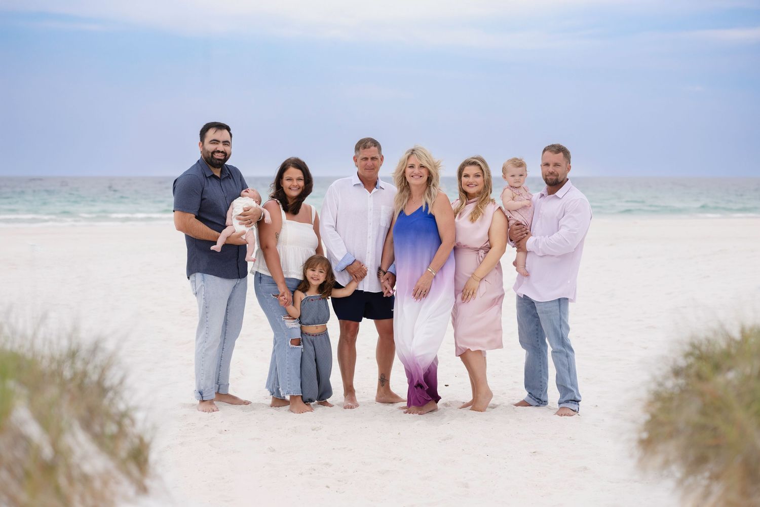 Multi-generational family portrait on a white sand beach with turquoise water, posing together on a sunny day.