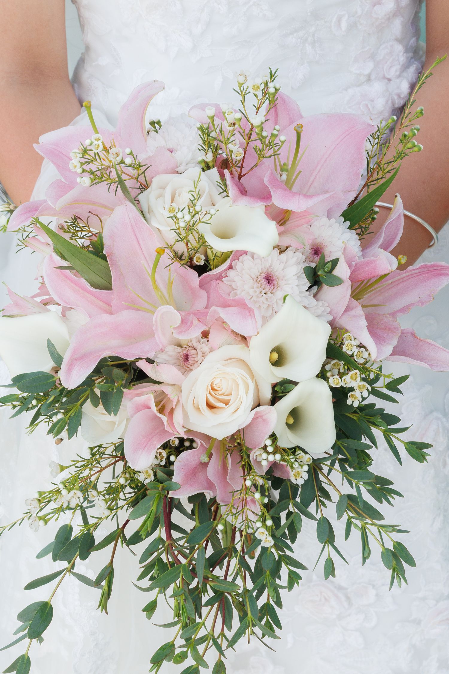 Bride holding a cascading wedding bouquet with pink lilies, white calla lilies, a cream rose, and greenery.