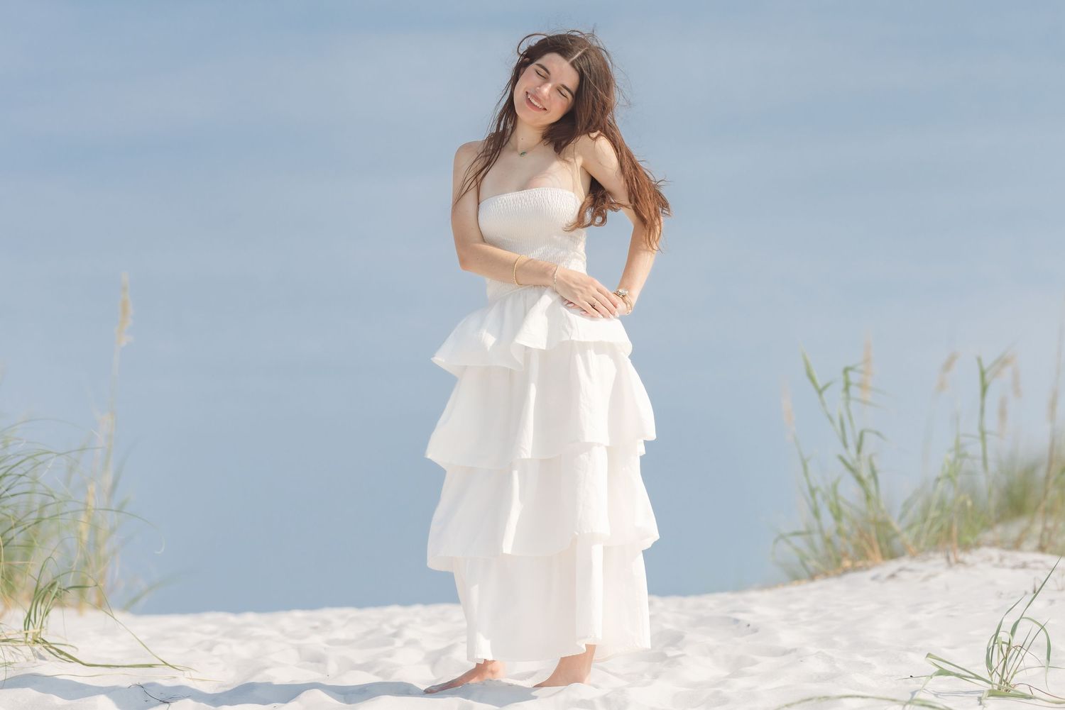 Young woman in white tiered strapless gown posing on white sand dunes at the beach.