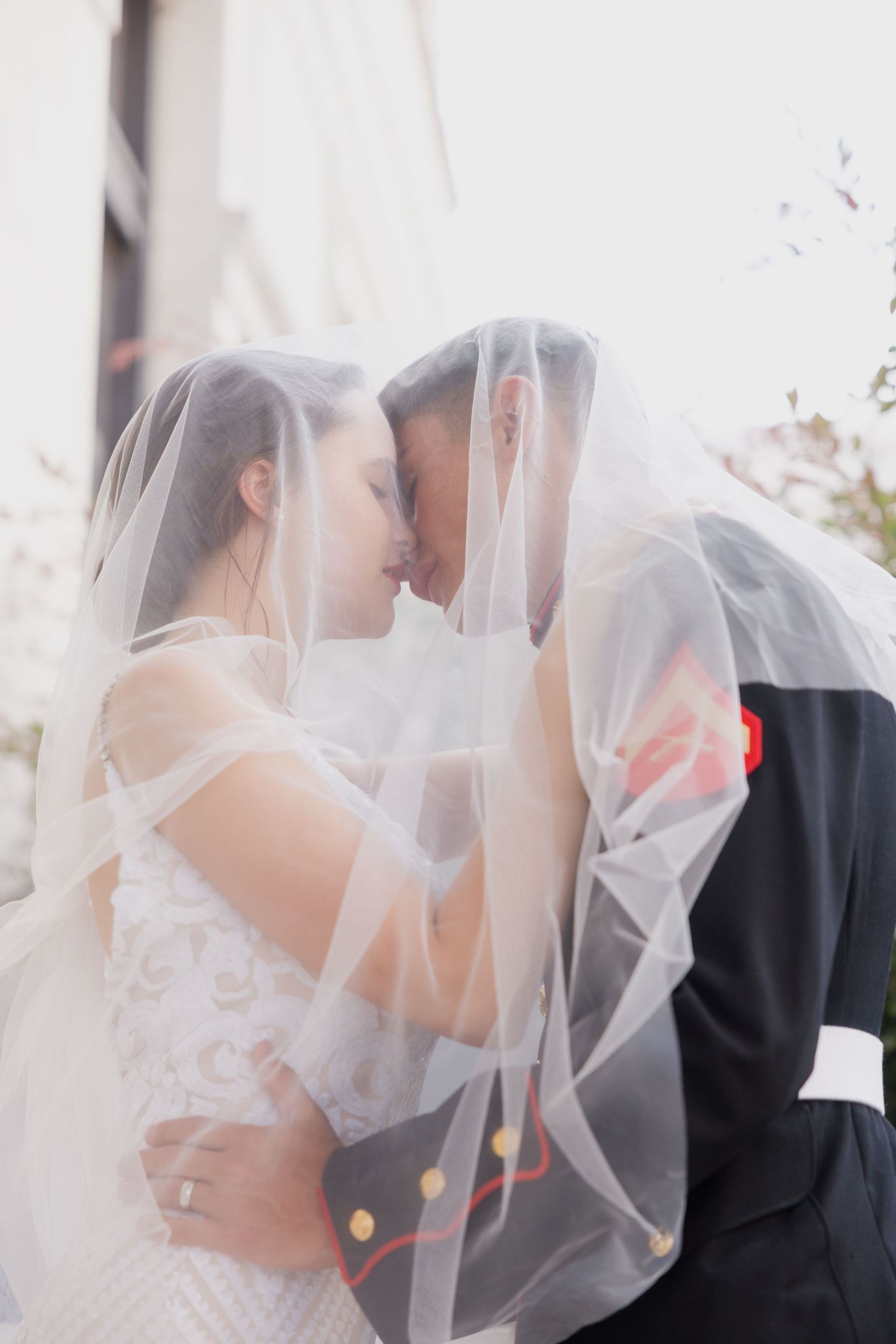 Bride and groom sharing an intimate kiss under a flowing white veil on their wedding day.