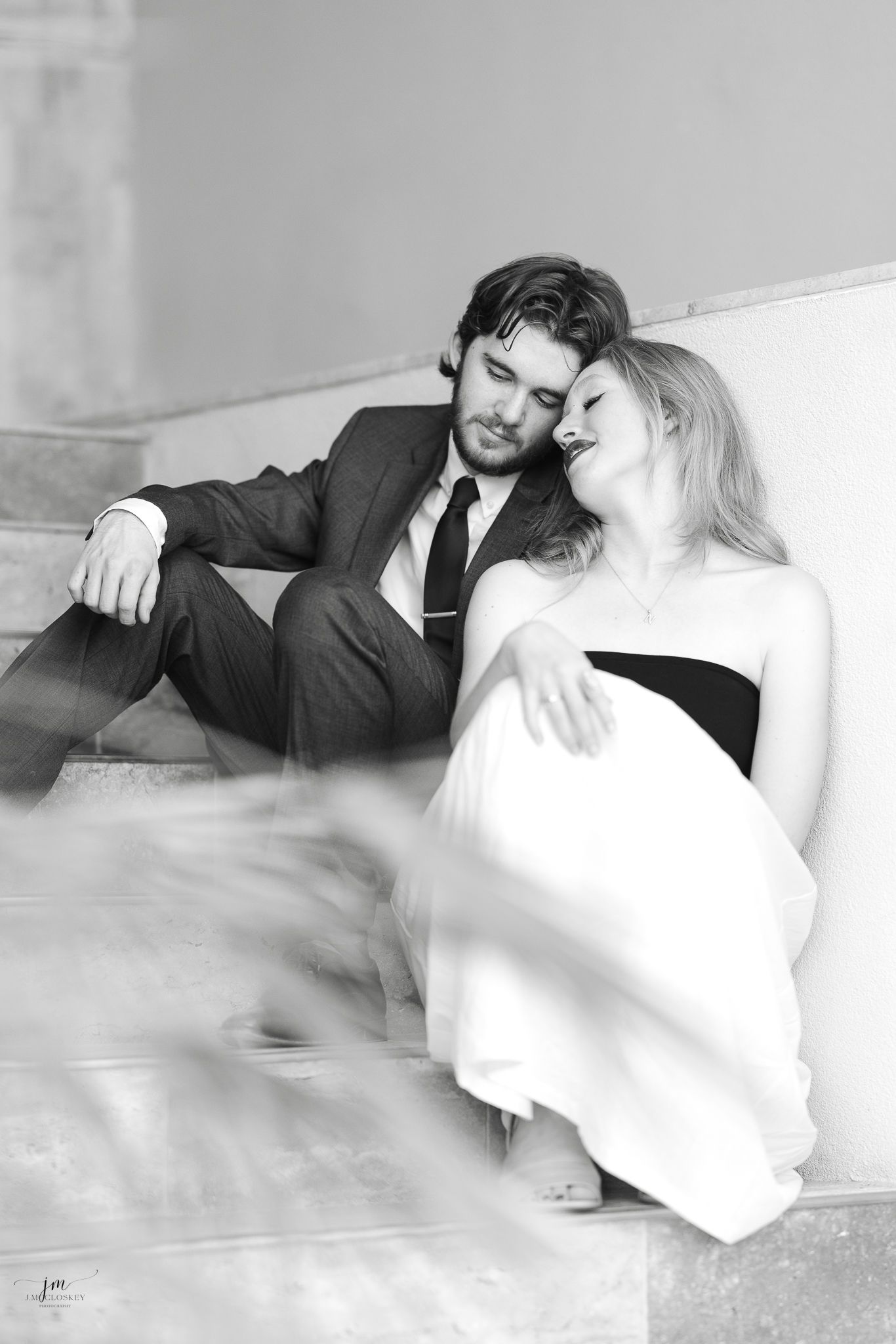 A black and white photo of a couple relaxing together on stone steps.
