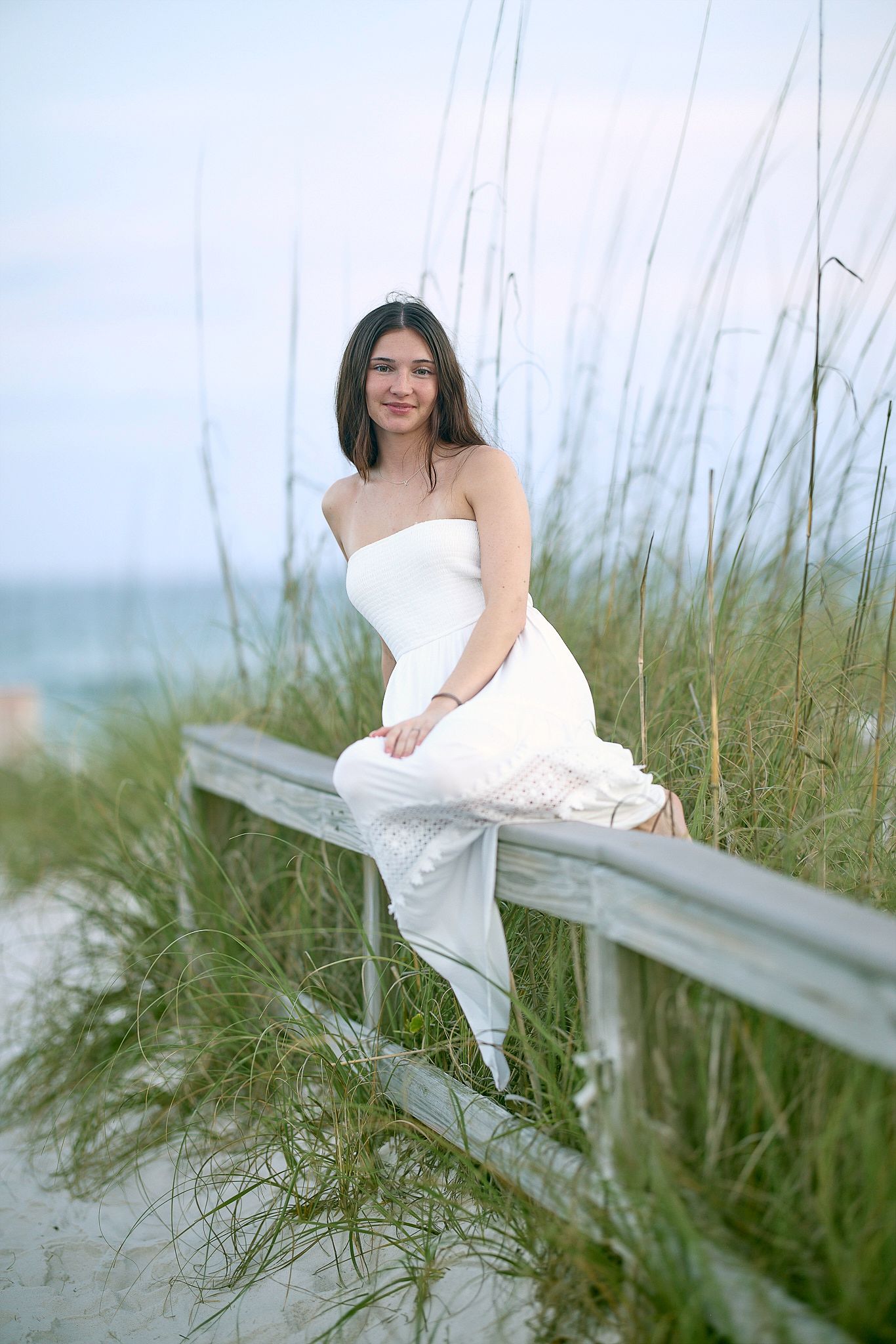 Coastal portrait on wooden railing with sea grass and ocean in background.