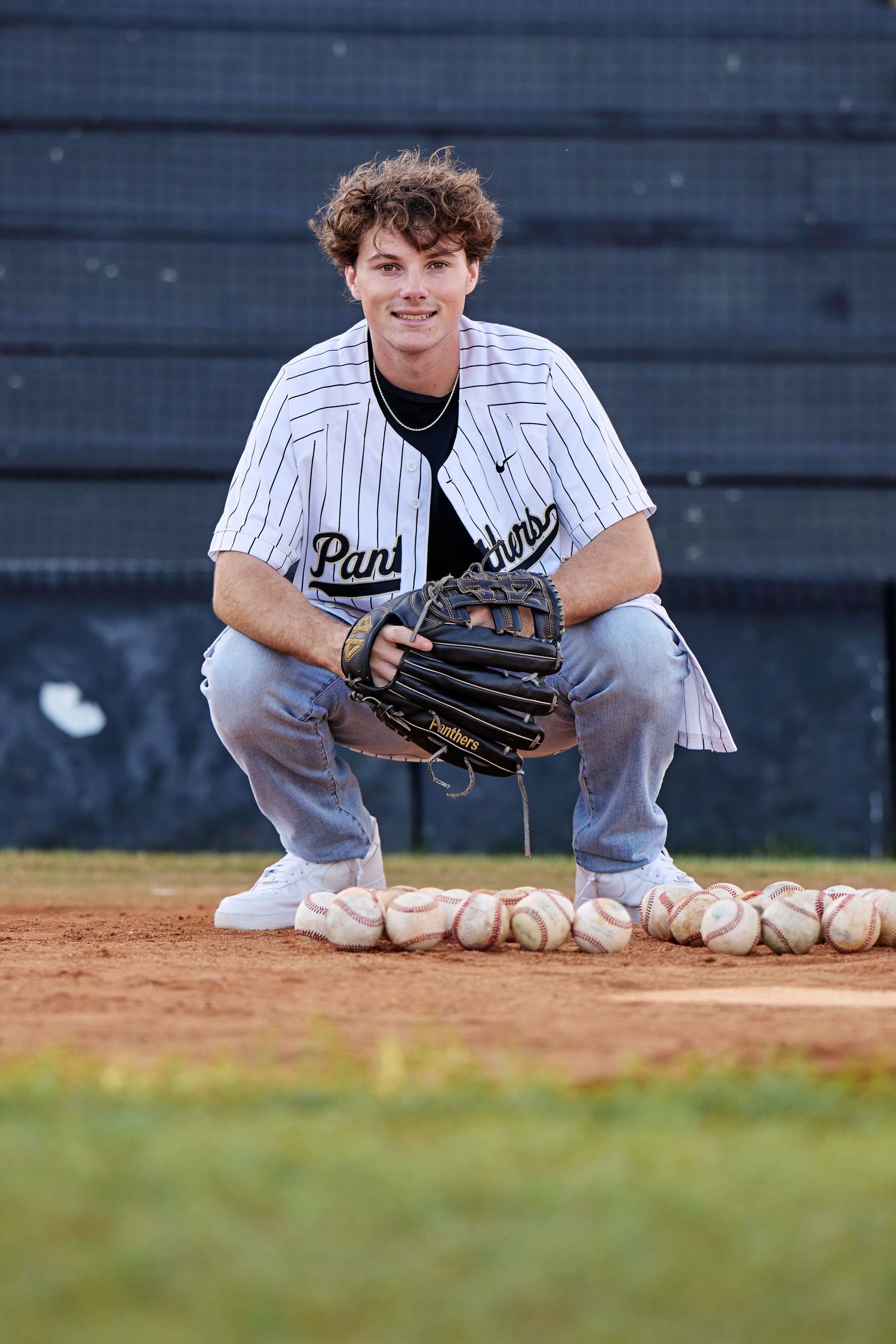 Baseball player in pinstripe uniform crouches on field with baseball glove and baseballs.