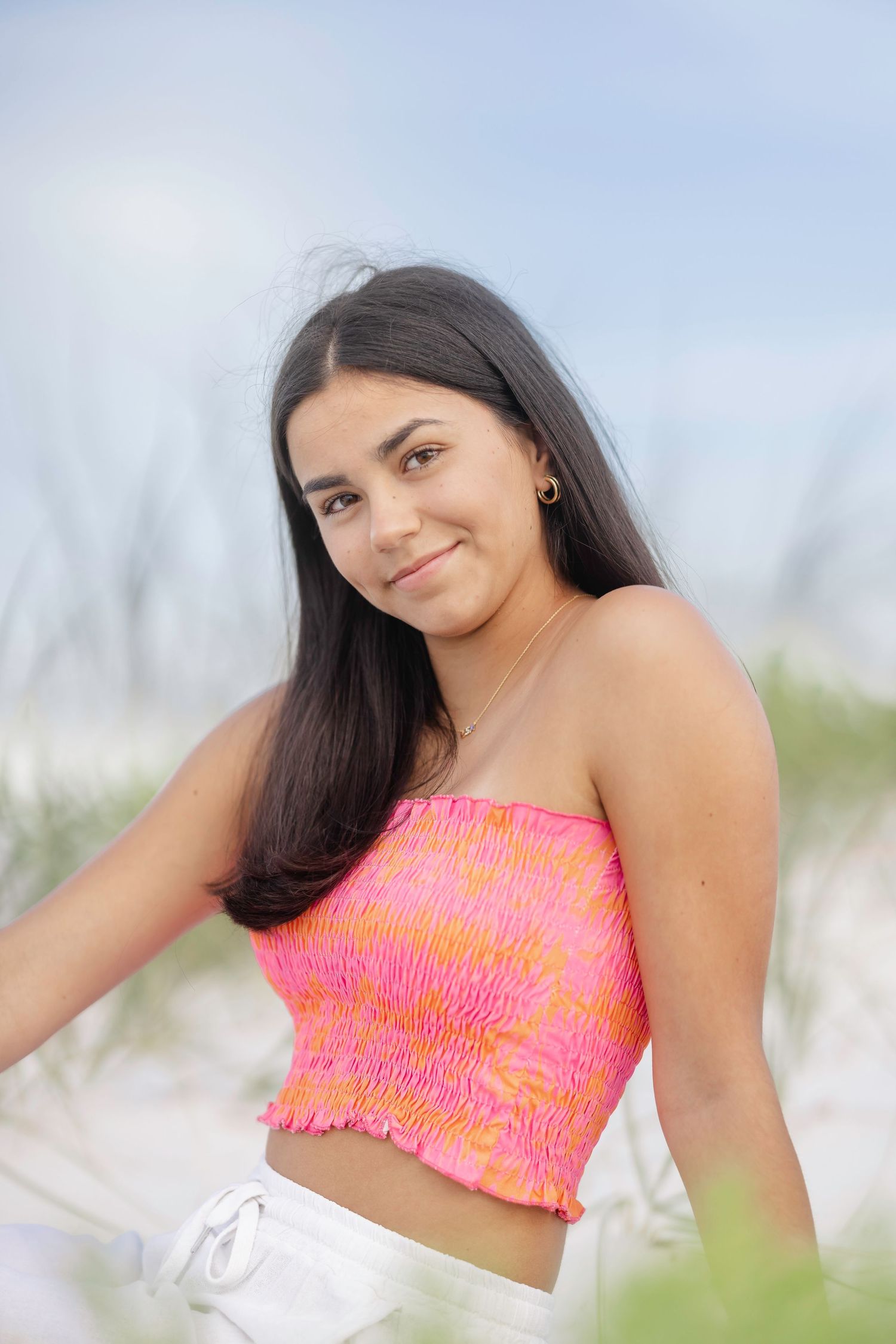Woman in coral pink crop top smiles brightly on beach with soft focus background.