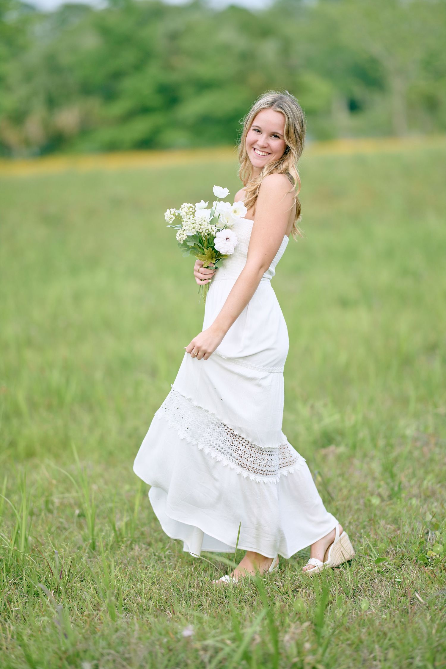 White boho dress twirls in meadow with wildflowers and summer greenery.