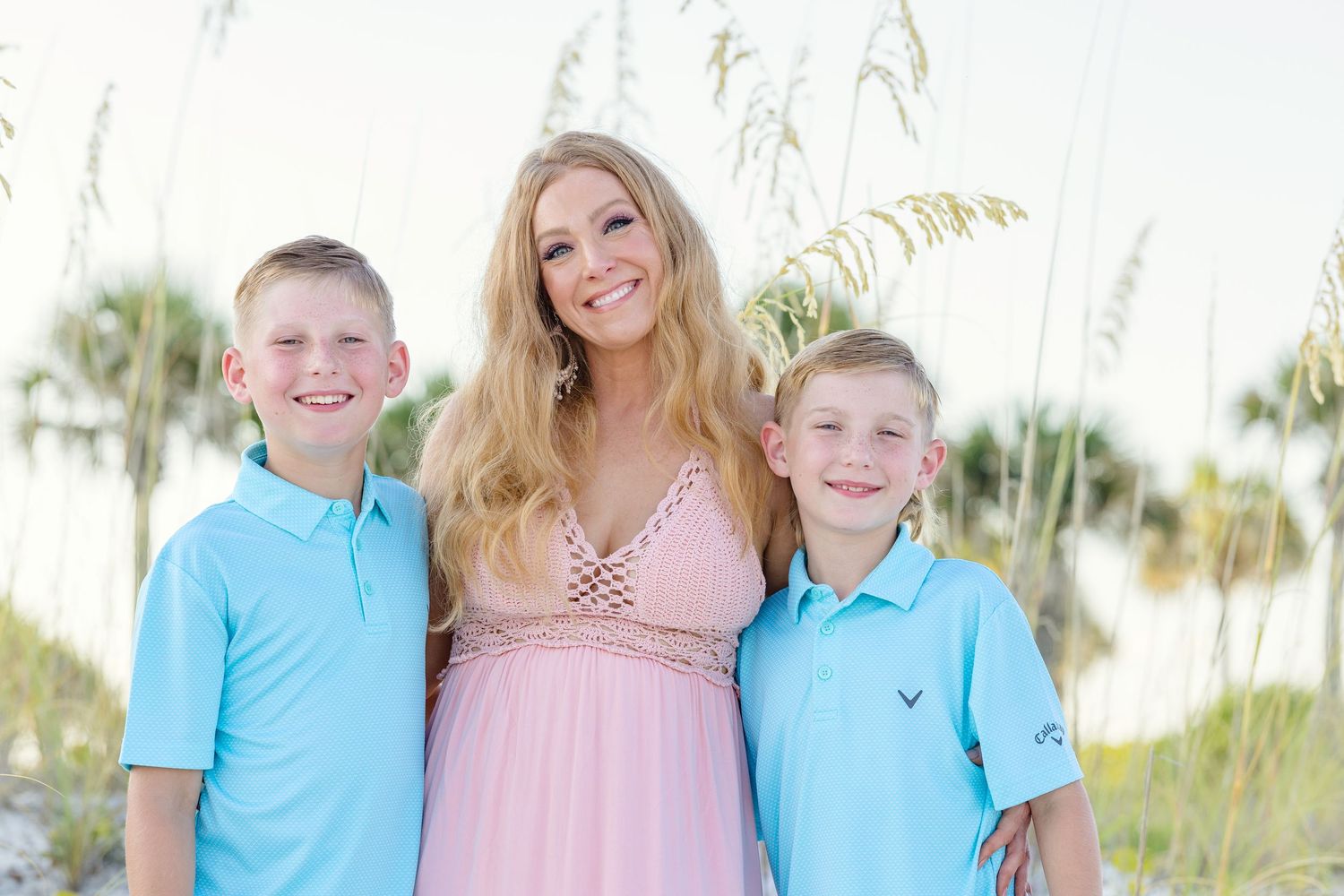 A family wearing coordinated blue and pink outfits poses outdoors near palm trees on a sunny day.