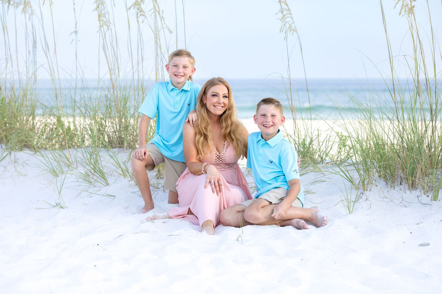 Family relaxing on white sand with sea oats and ocean in background.