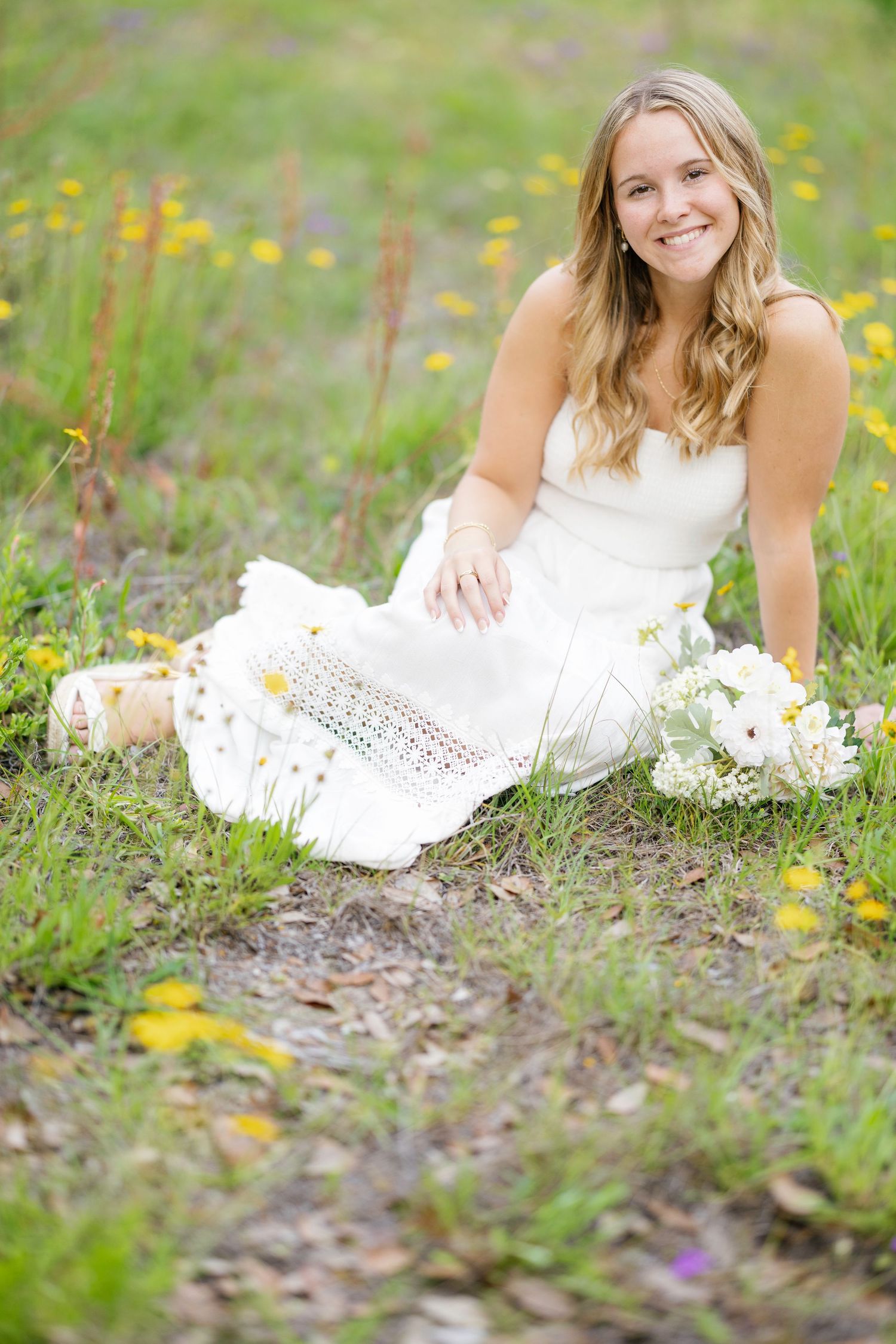 A woman in a white dress lies in a field of yellow wildflowers during a spring photoshoot.