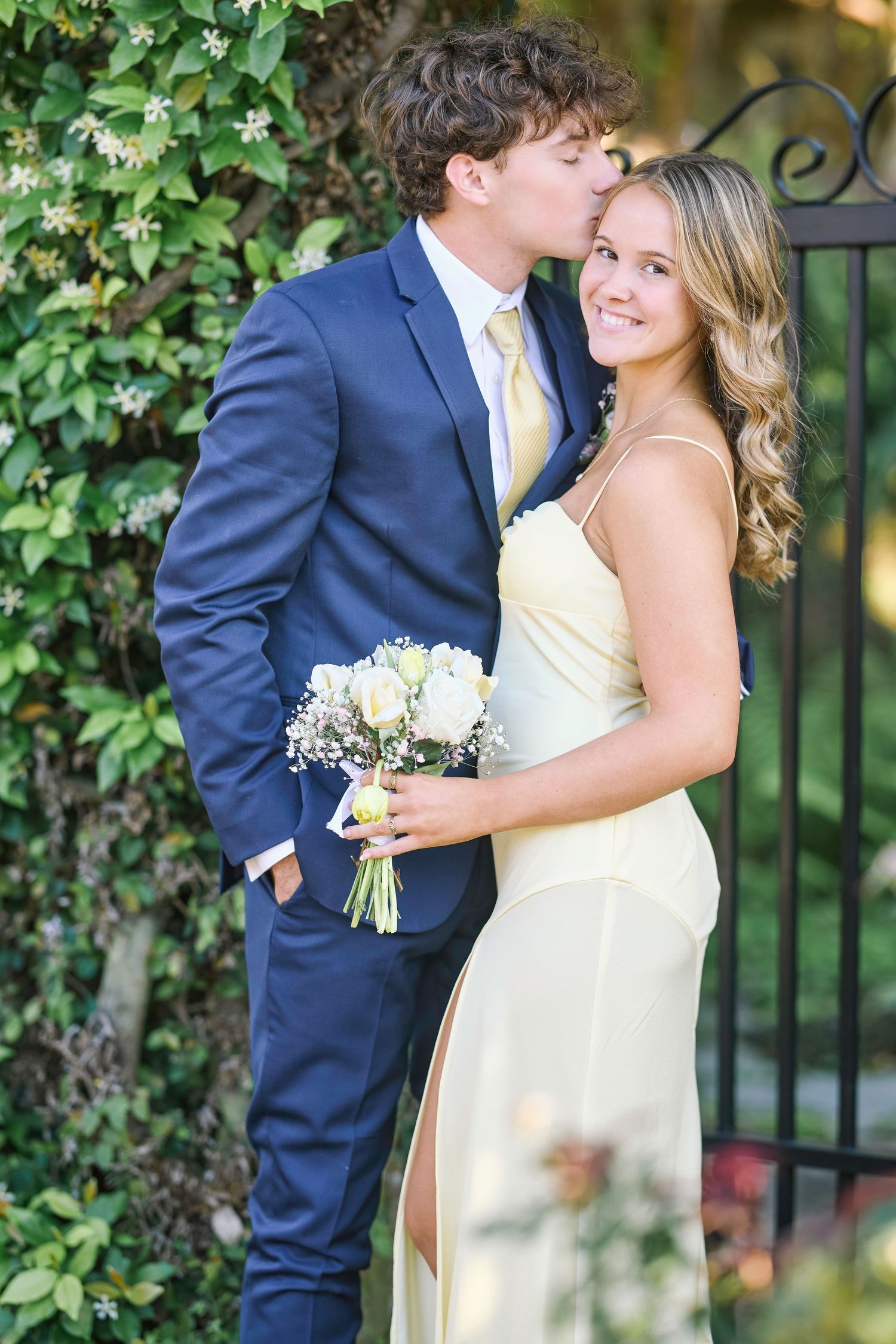 A romantic wedding couple poses together against a lush green ivy wall backdrop in formal attire.