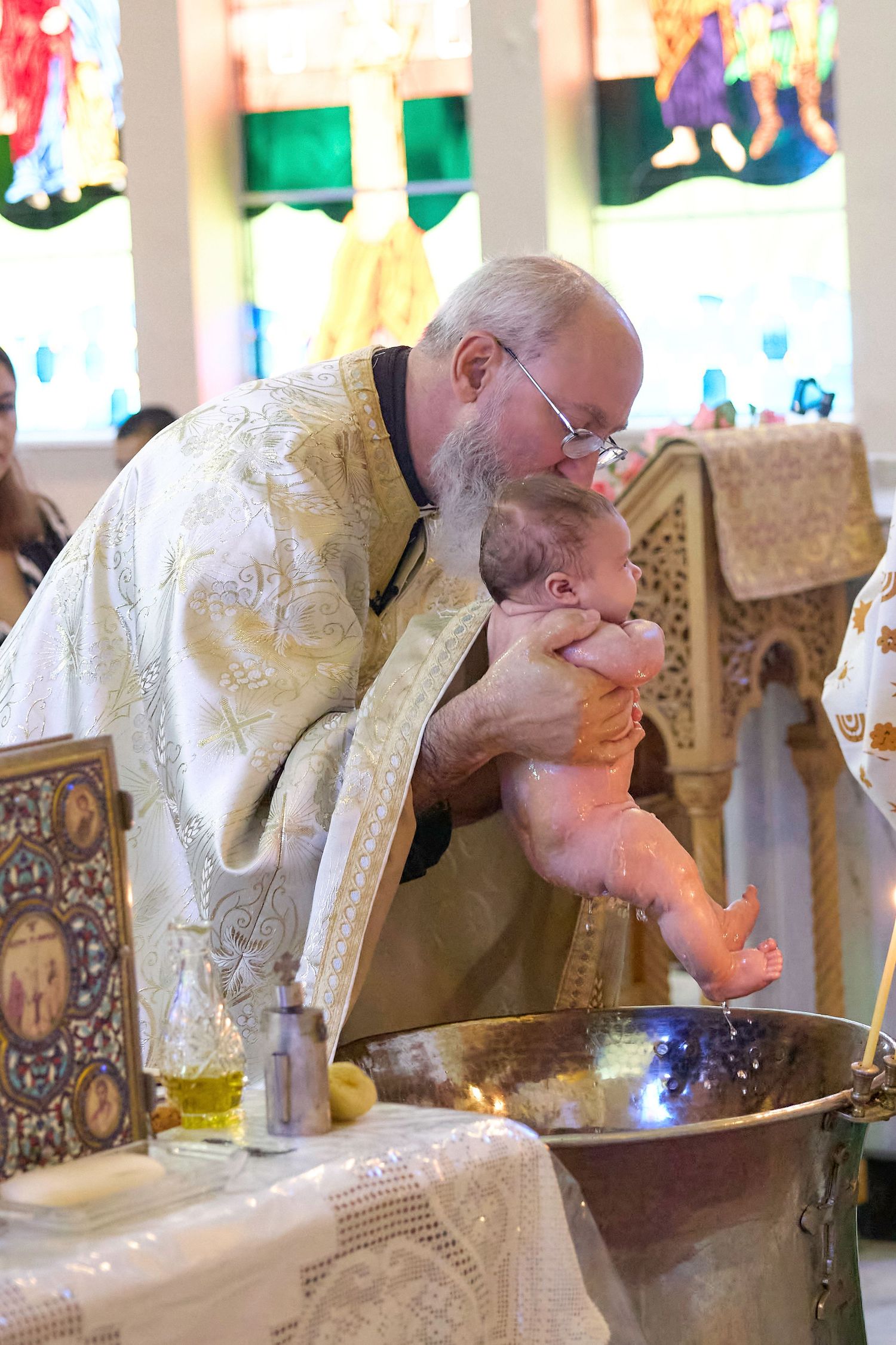 Priest in white and gold vestments bends to kiss a religious artifact during a ceremonial ritual.