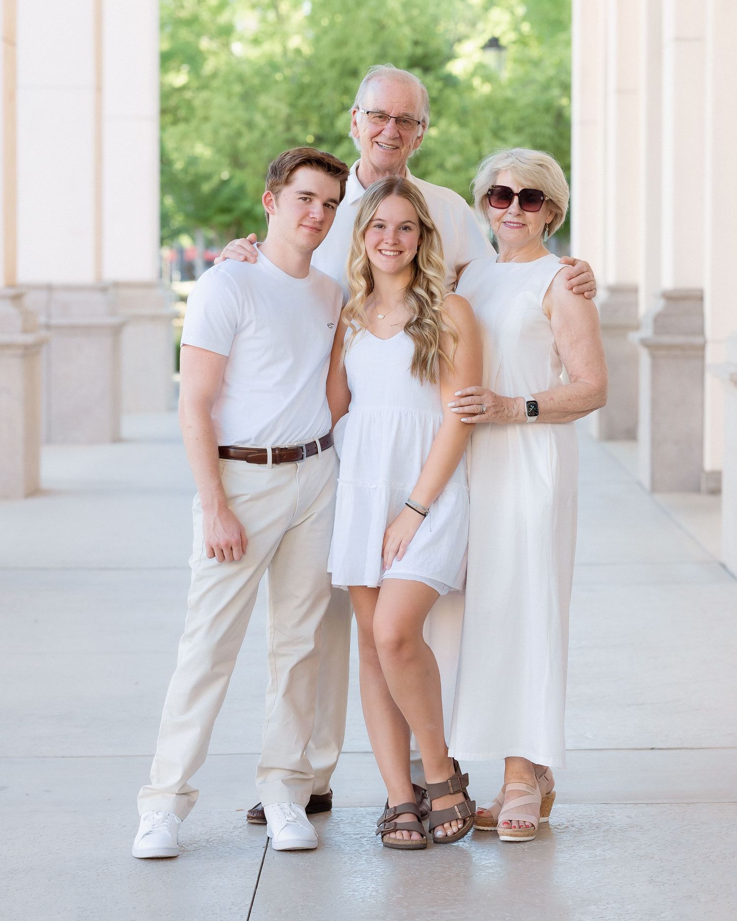 Family of four posing in white outfits outdoors near stone columns.
