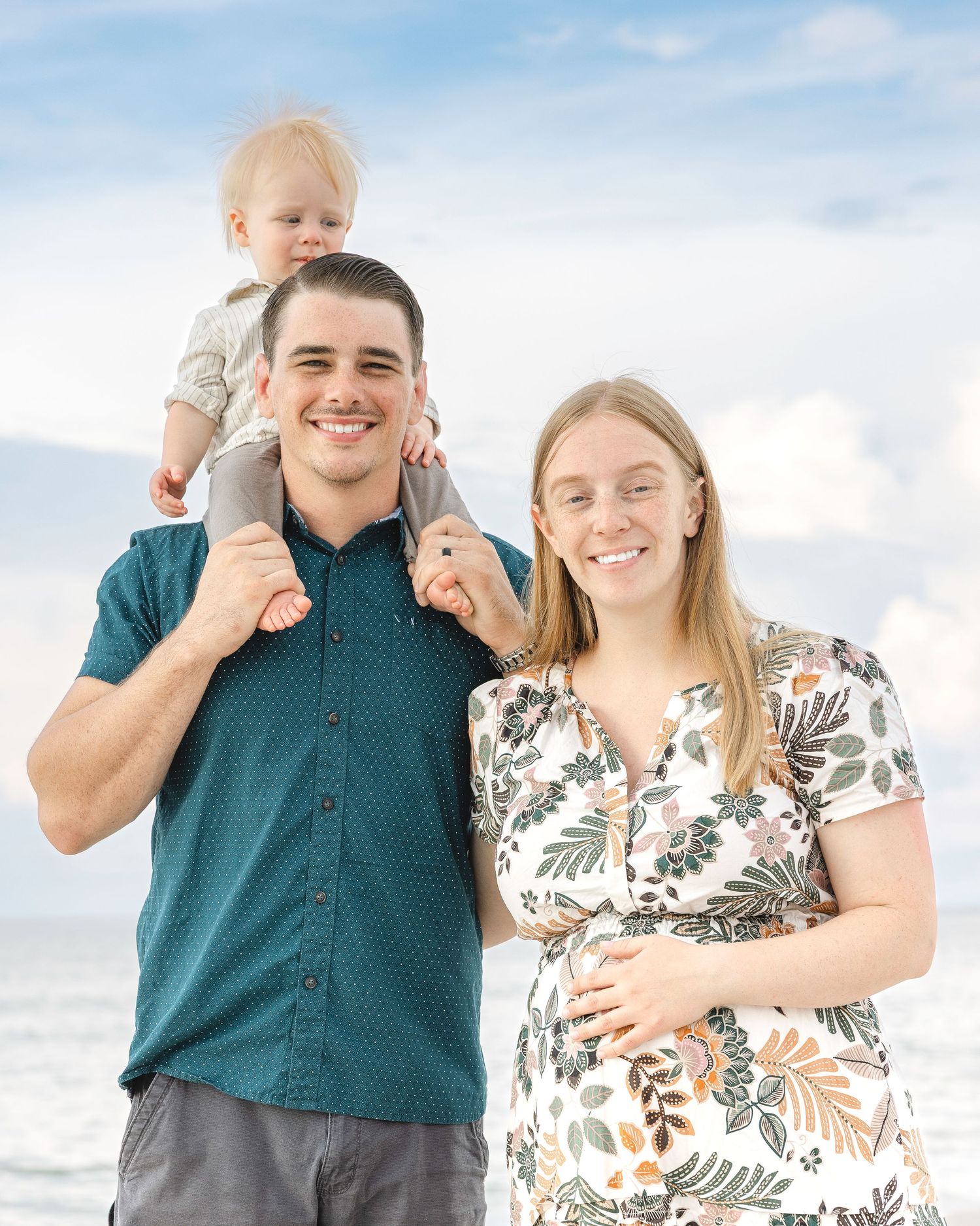 Beach portraits in casual attire against bright blue sky and white clouds.