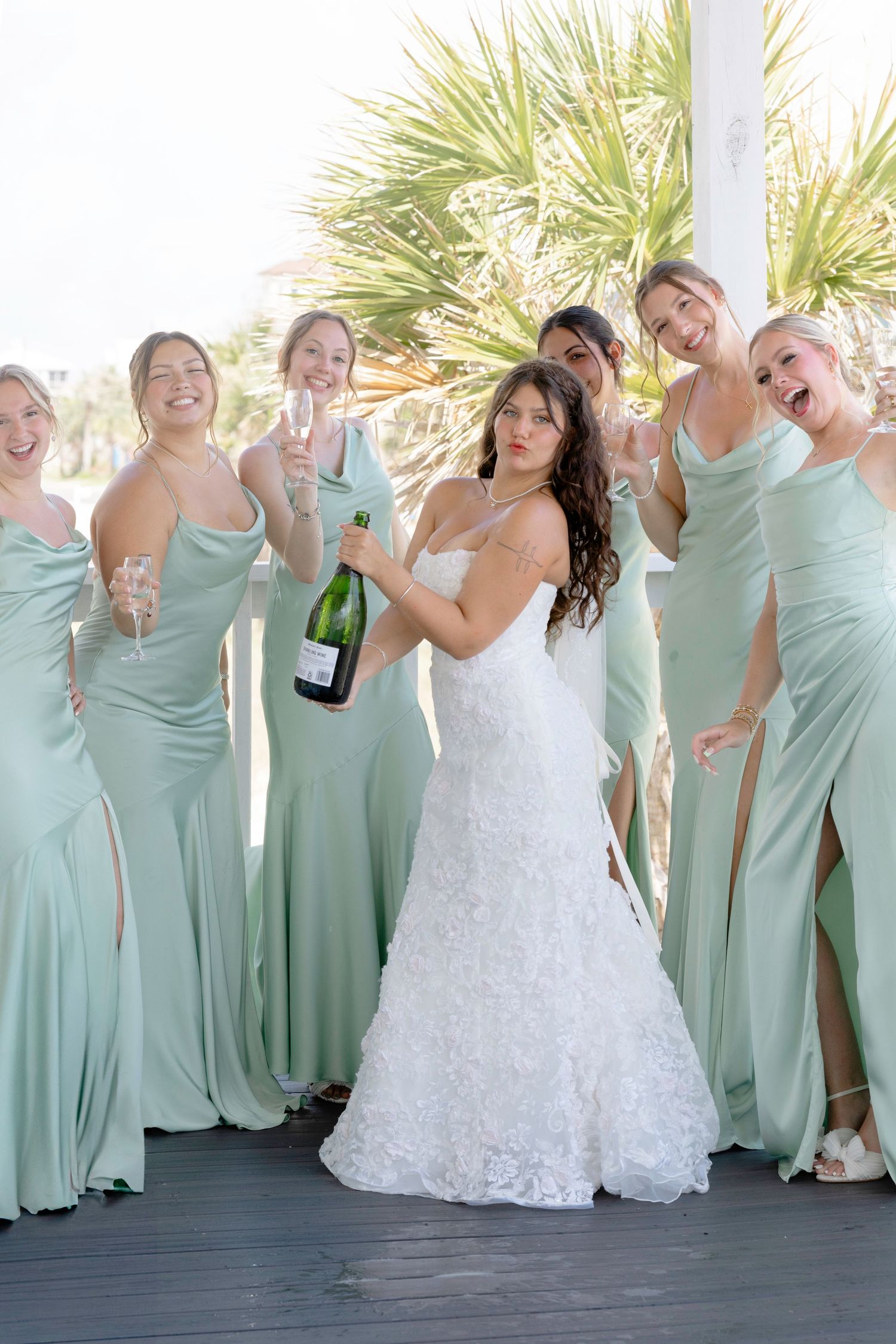 Wedding party in mint green bridesmaid dresses and white bridal gown pose together with laughter.