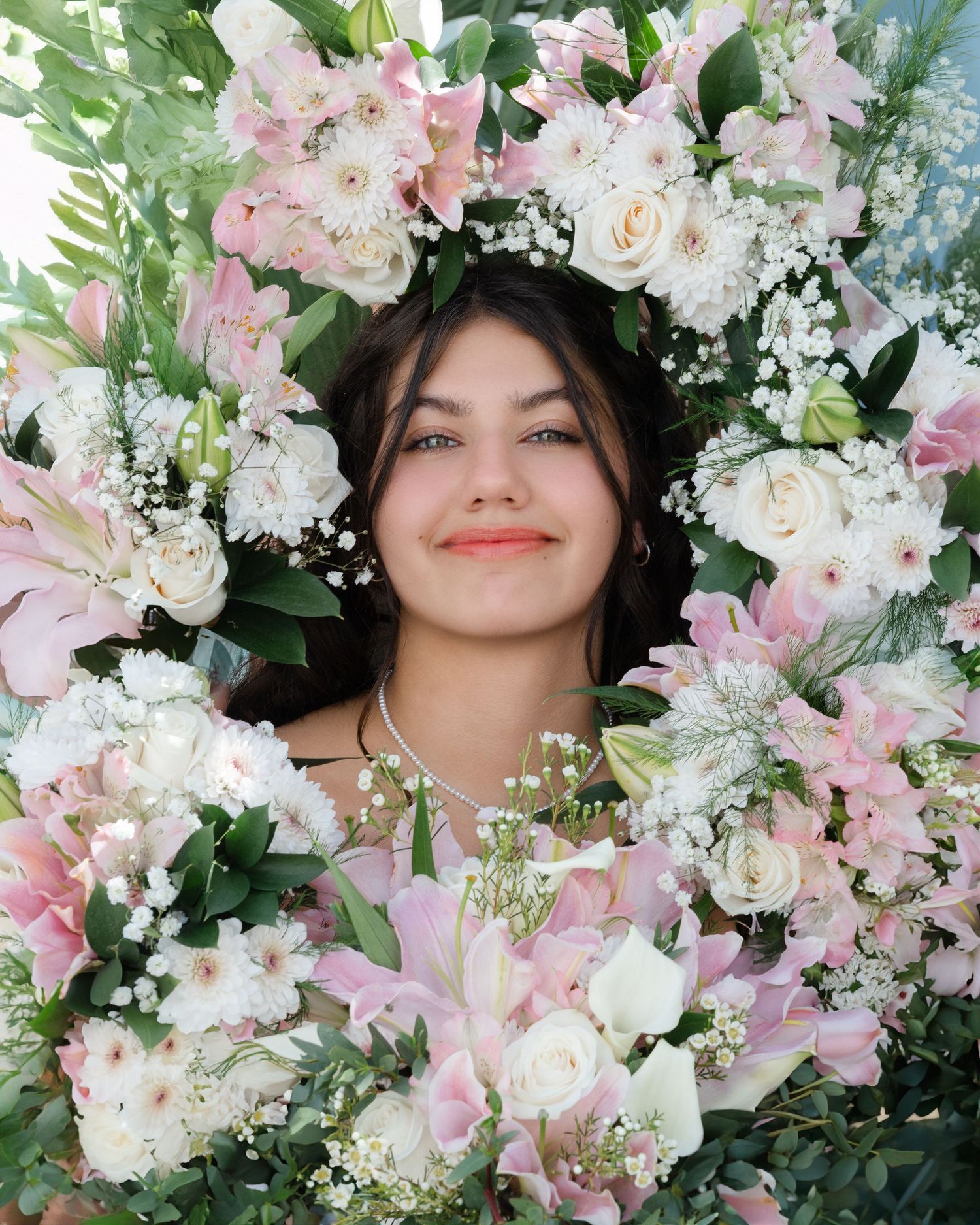 Young woman smiling, surrounded by lush pink and white floral arrangement with roses and lilies.