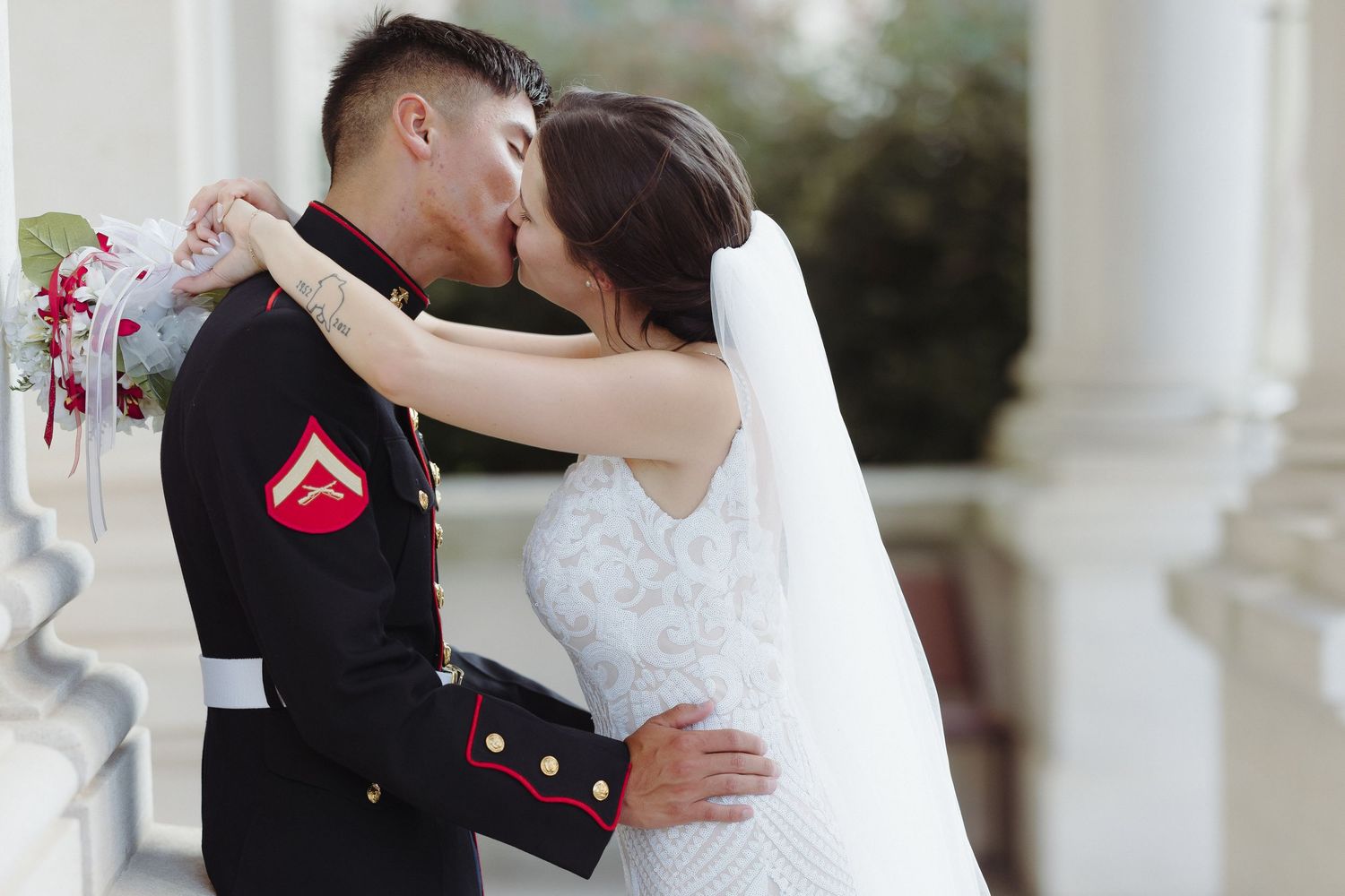 A Marine in dress uniform shares a romantic kiss with his bride in a white lace gown during their wedding day.