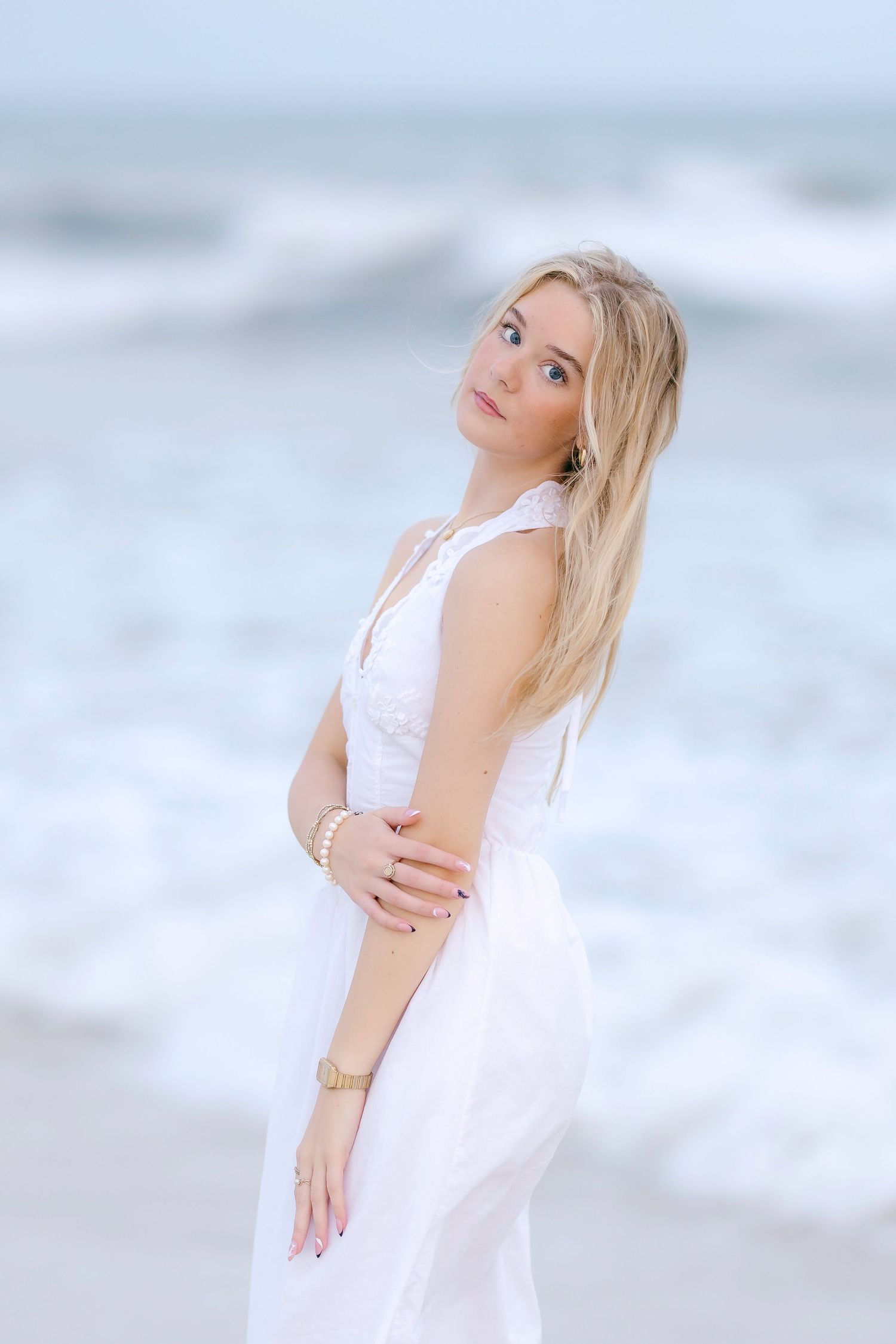 Dreamy coastal portrait featuring white dress against misty ocean waves.