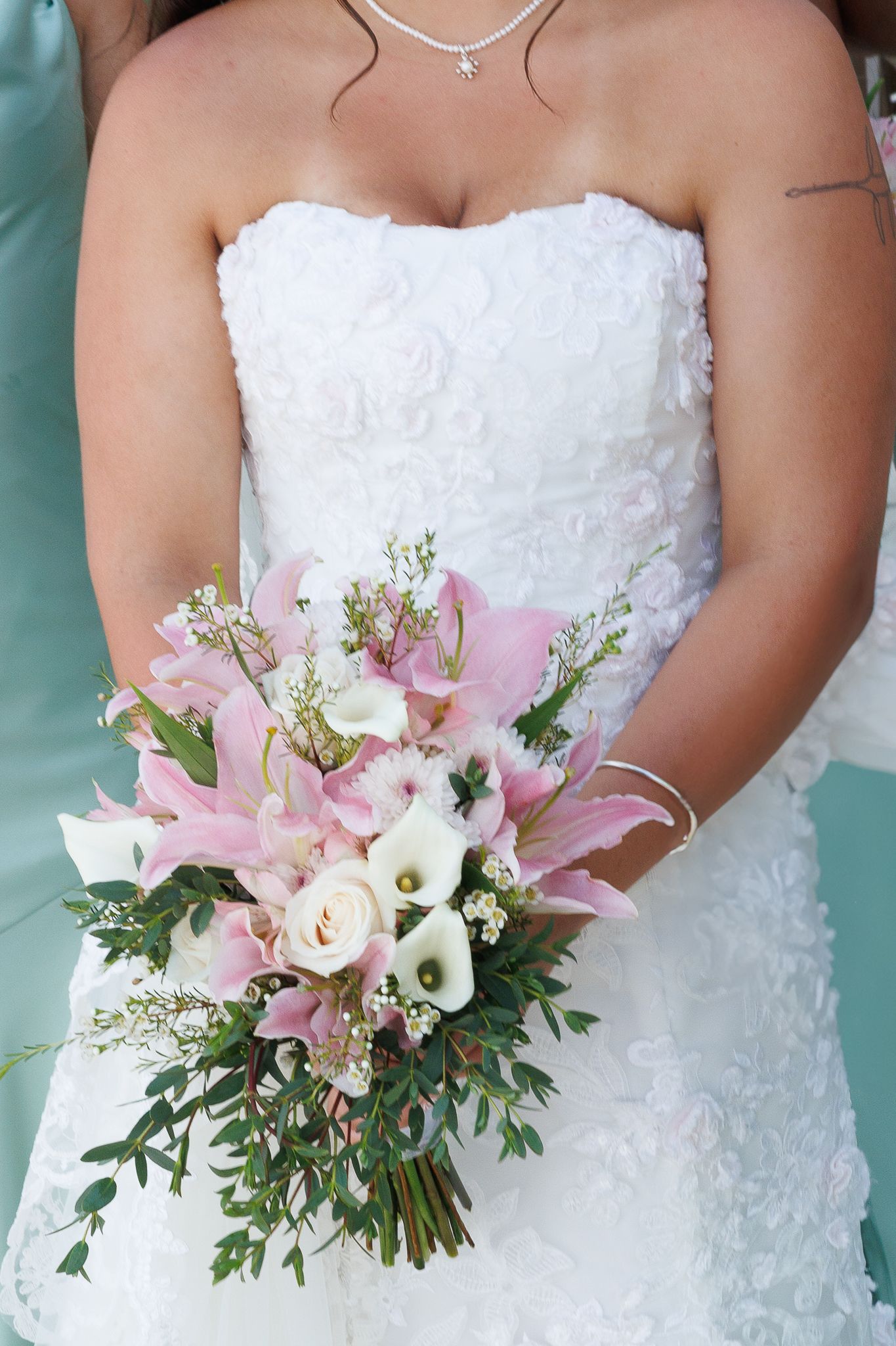Close-up of white wedding dress with pink and white floral bouquet.