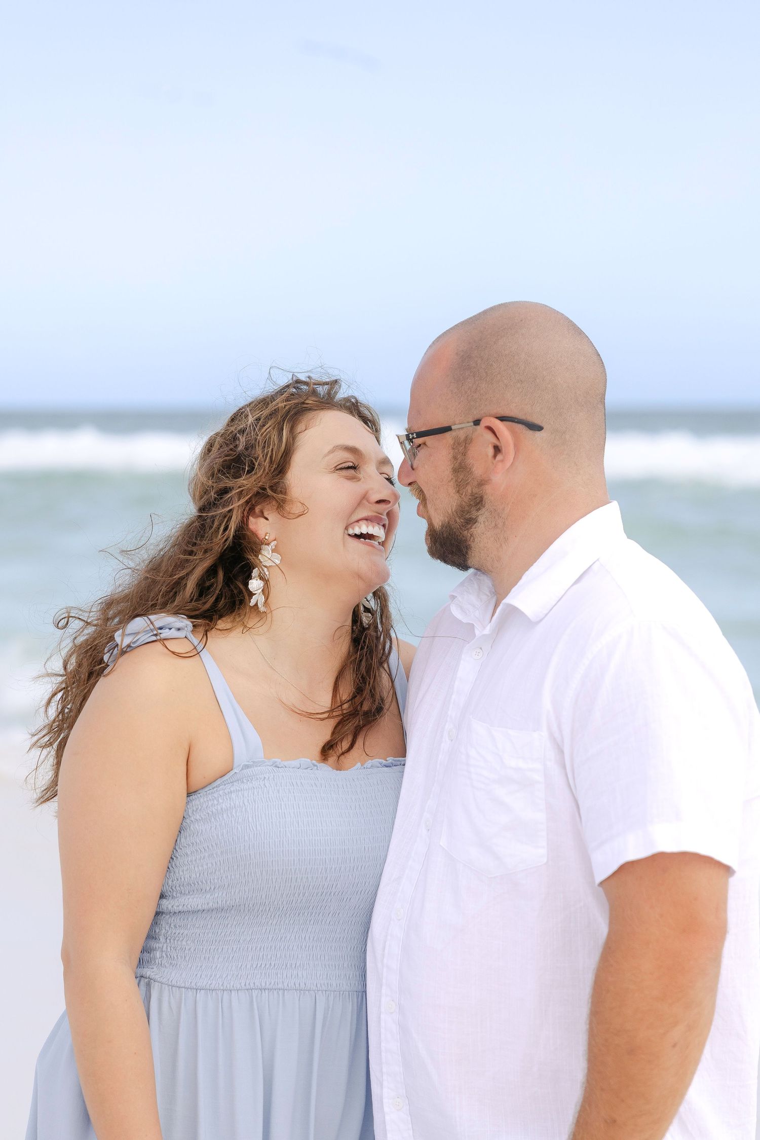 Couple sharing laughter together on a bright sunny beach in casual summer attire.