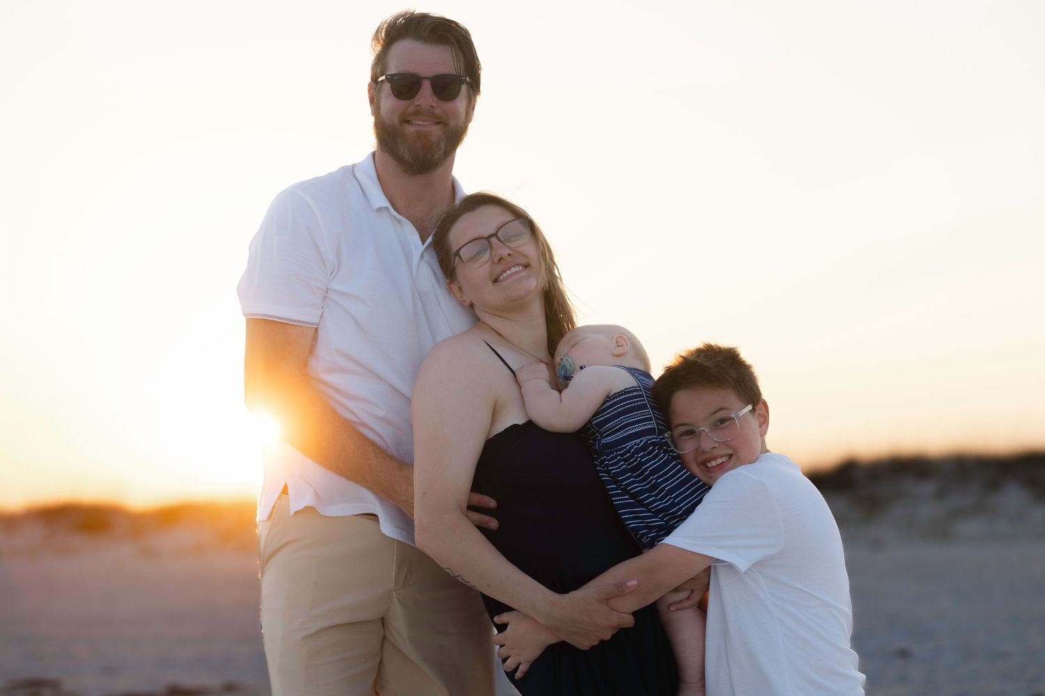 Family of three sharing warm embrace on beach at golden sunset, parents and young son together.
