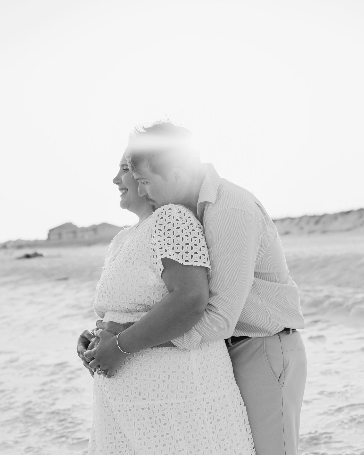 A black and white photo of a couple in a tender embrace on a beach.