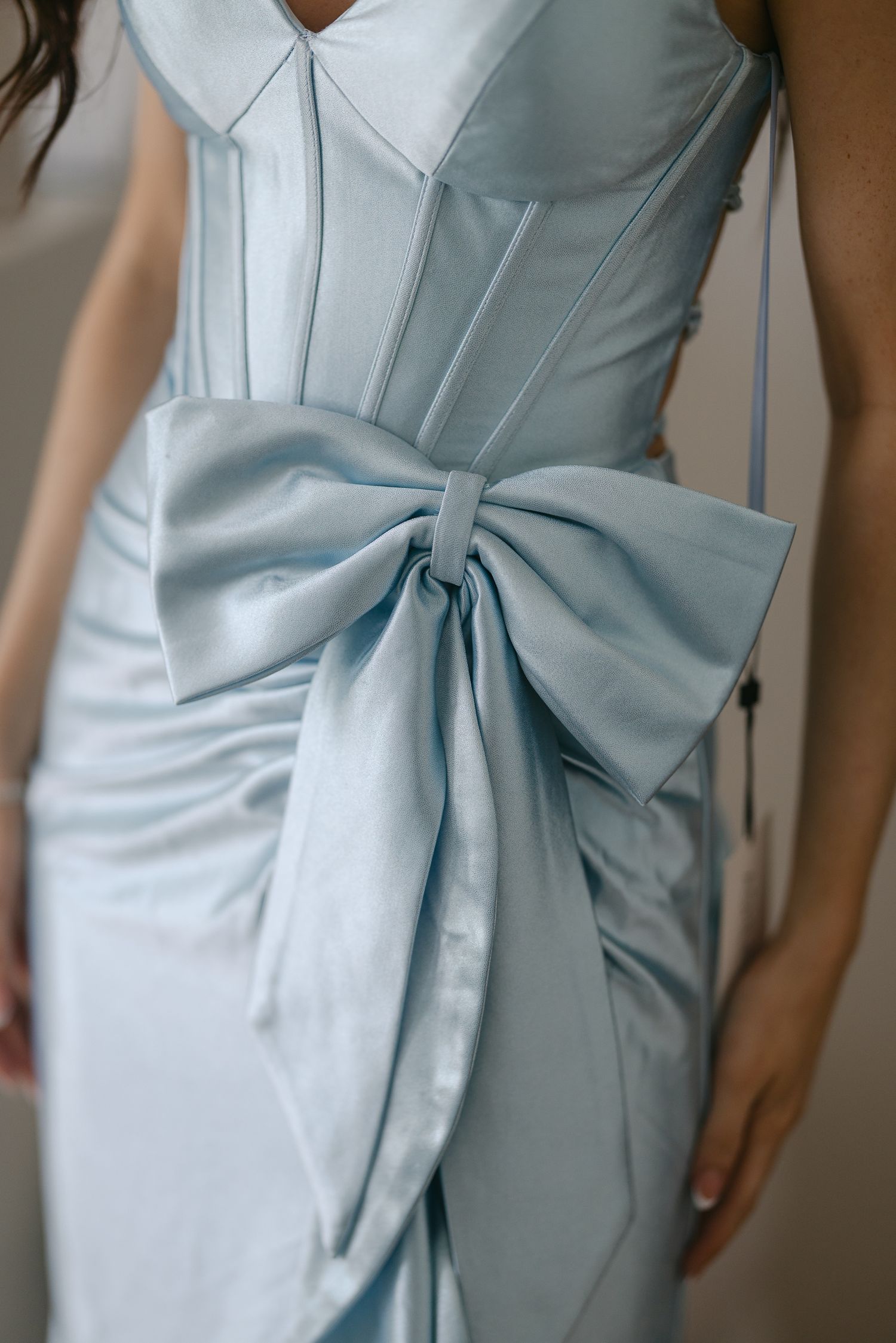 Detail of light blue satin dress featuring structured bodice and dramatic side bow.