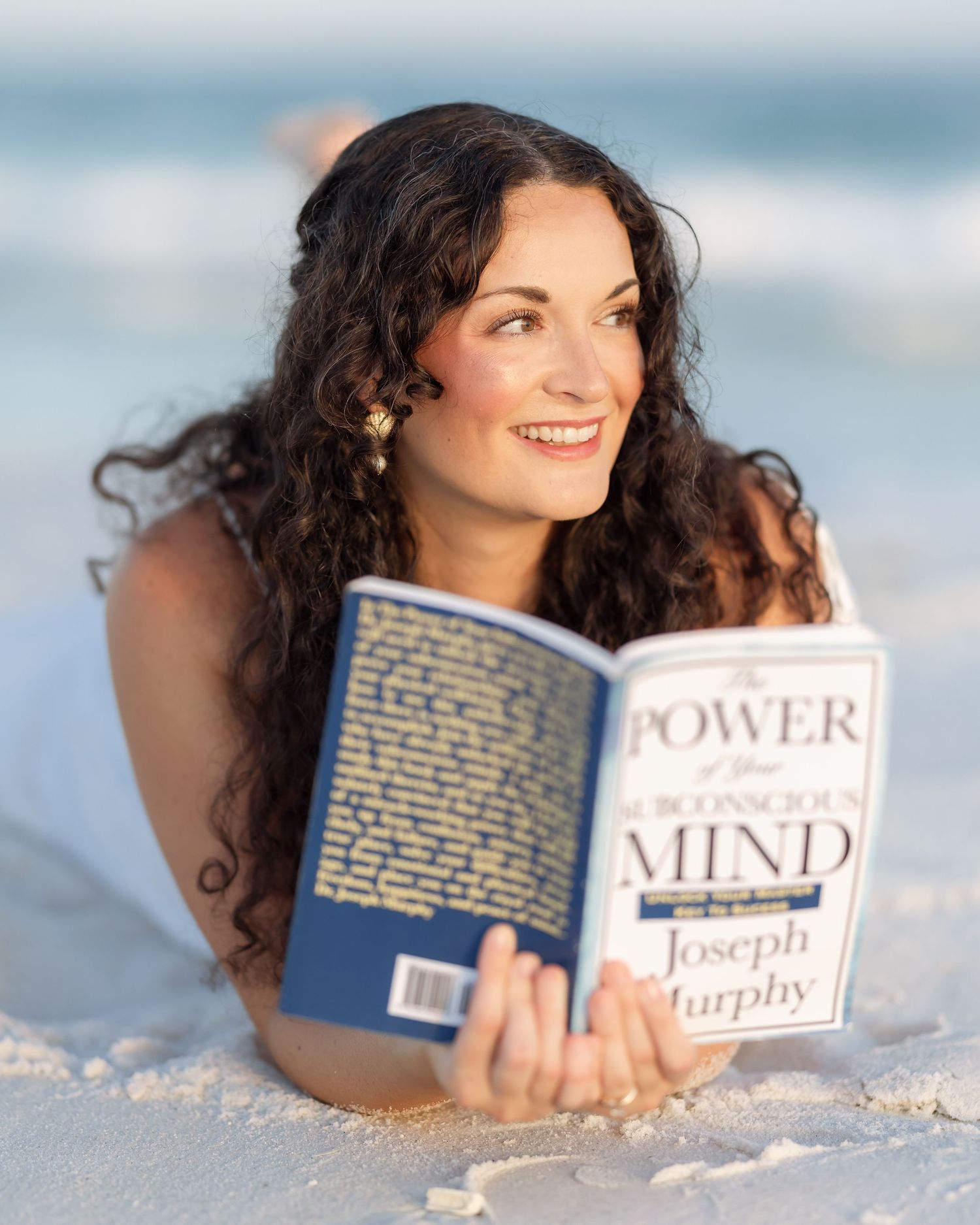 Woman reading The Power of Your Subconscious Mind book on a beach.