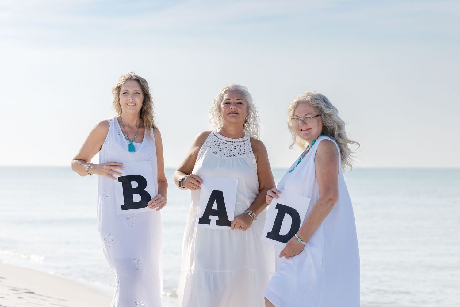 A group wearing white outfits poses together on a sunny beach while spelling out the word 'DAD' with letters.
