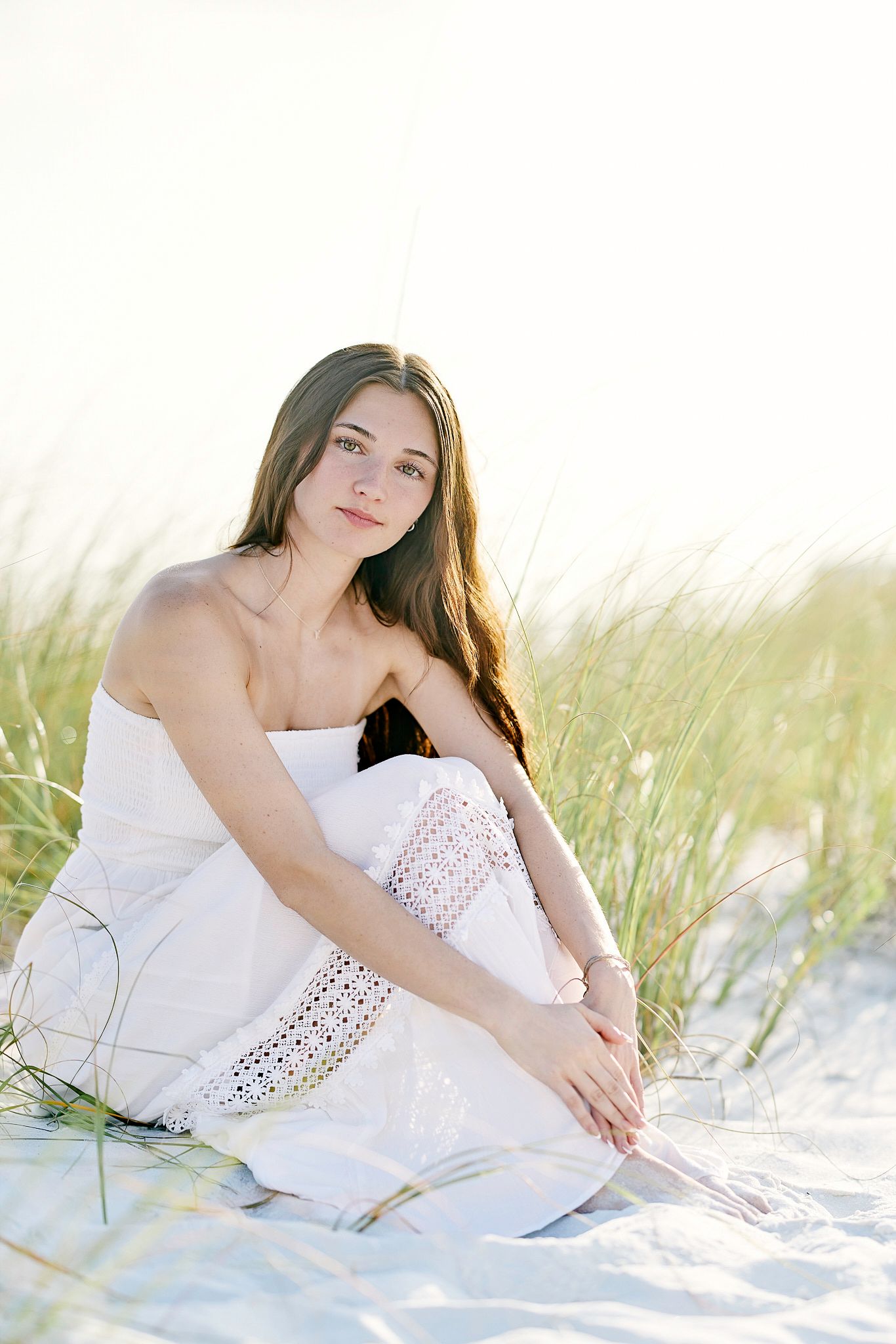 A white lace dress on a sandy beach with beach grass in soft golden light.