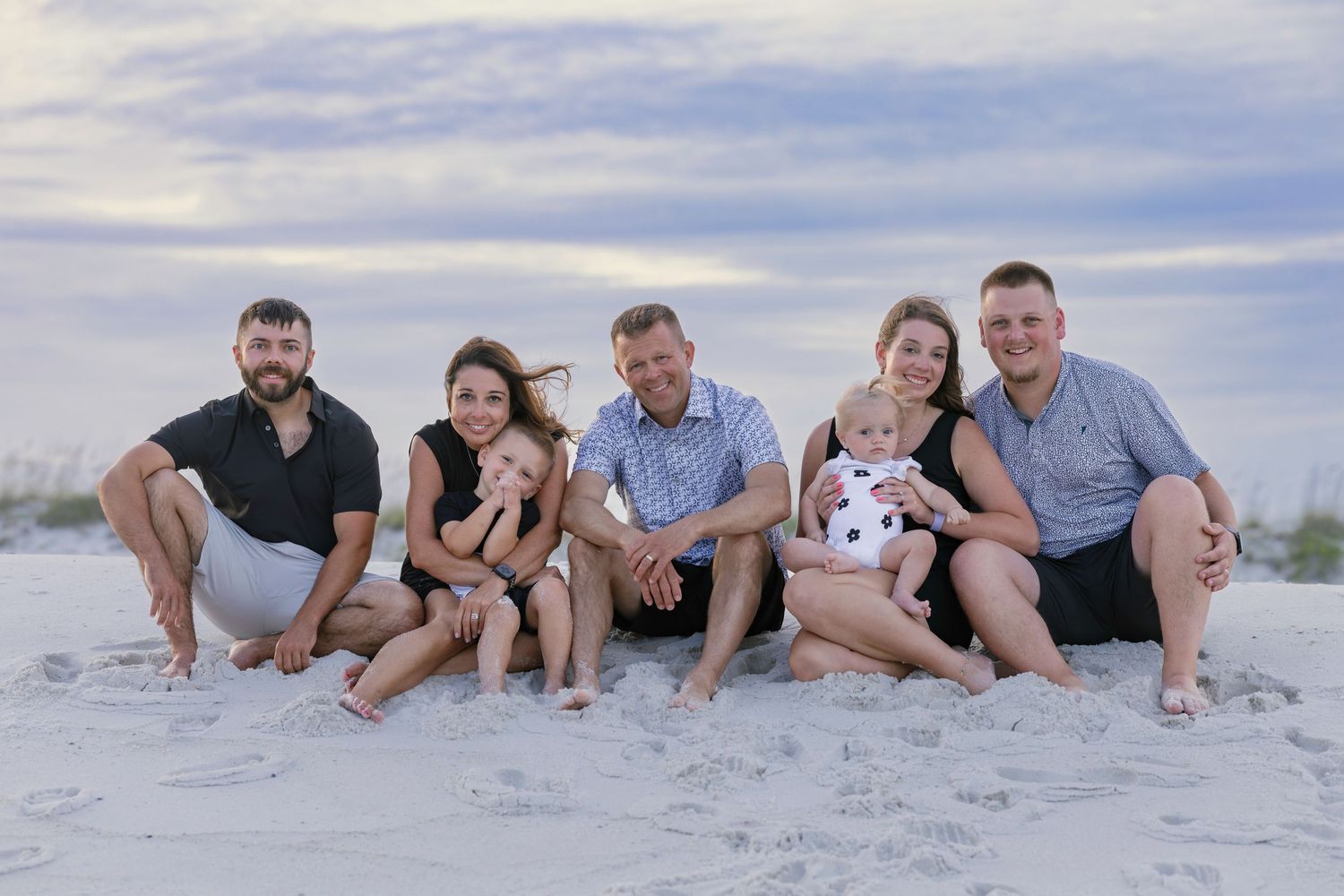 Family of seven posing together on a sandy beach at sunset, smiling for a portrait photo.