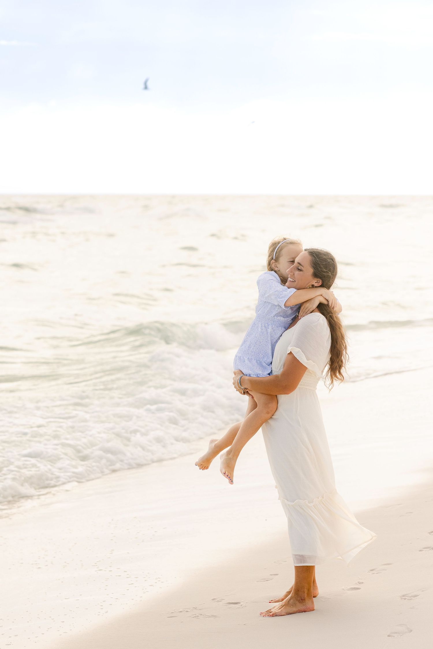 Romantic beach photoshoot with couple dancing and embracing by ocean waves at sunset.