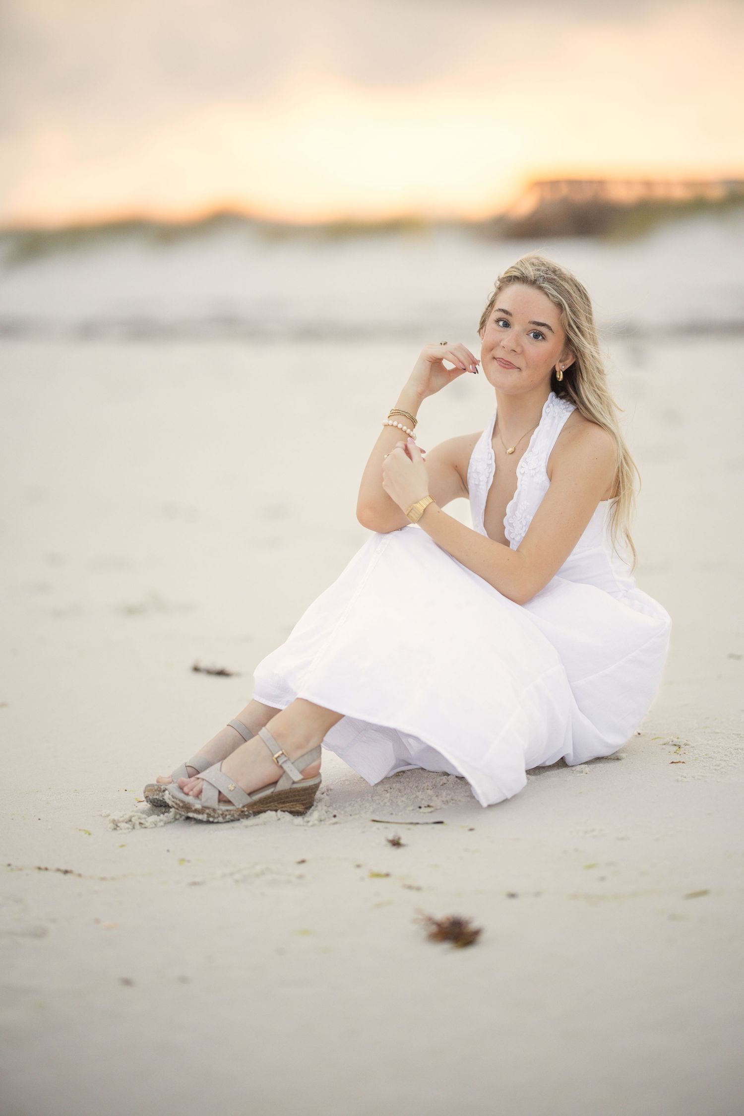 A person in a flowing white dress poses gracefully on a sandy beach during golden hour.