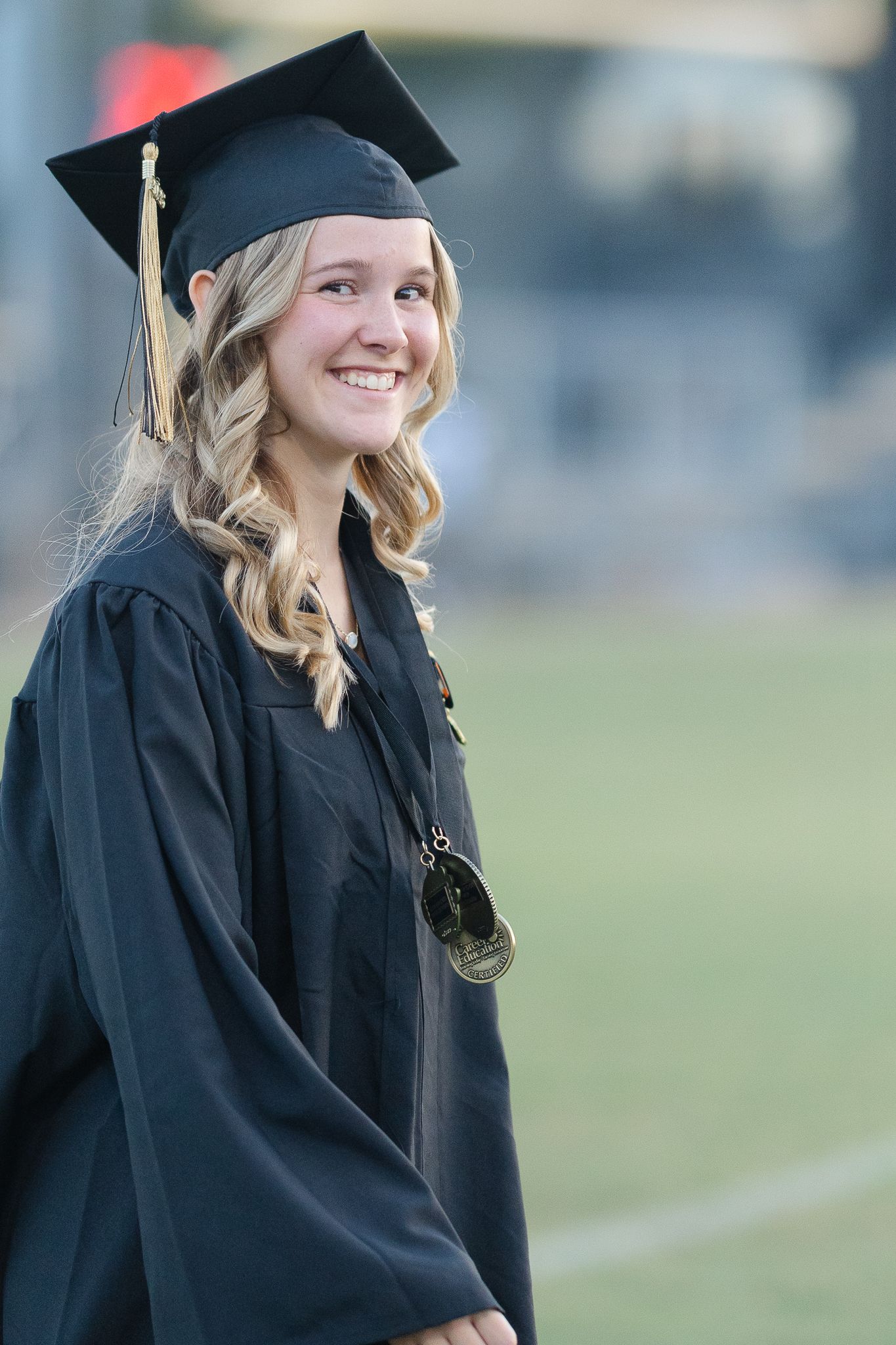 A graduate wearing traditional academic regalia stands outdoors during commencement.