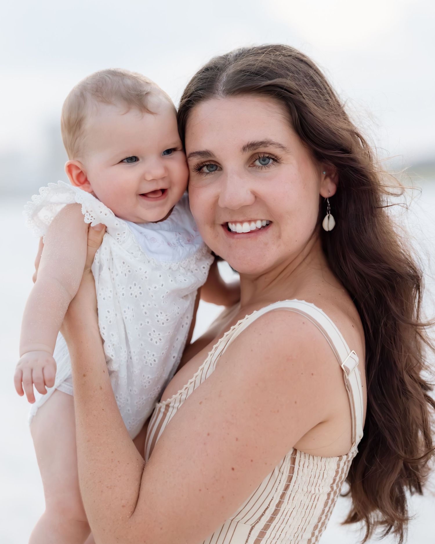 Smiling mother holds happy baby girl at sunny beach.