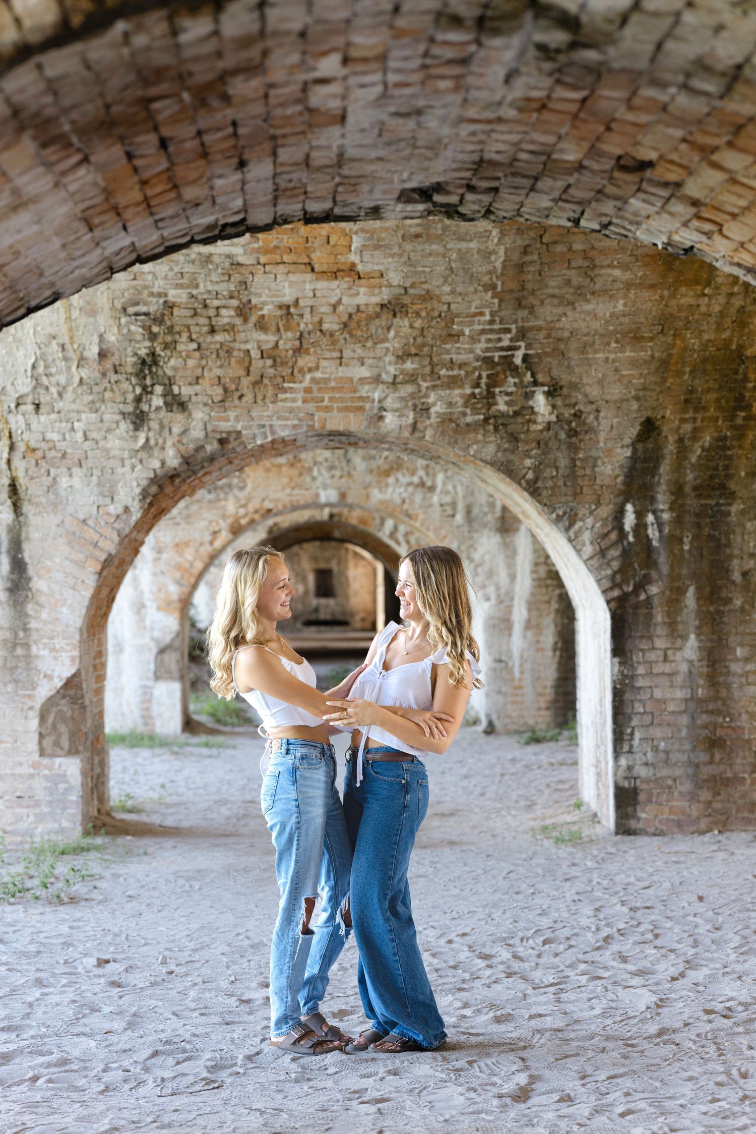 Two people share a tender moment under historic brick archways at a fort or castle.