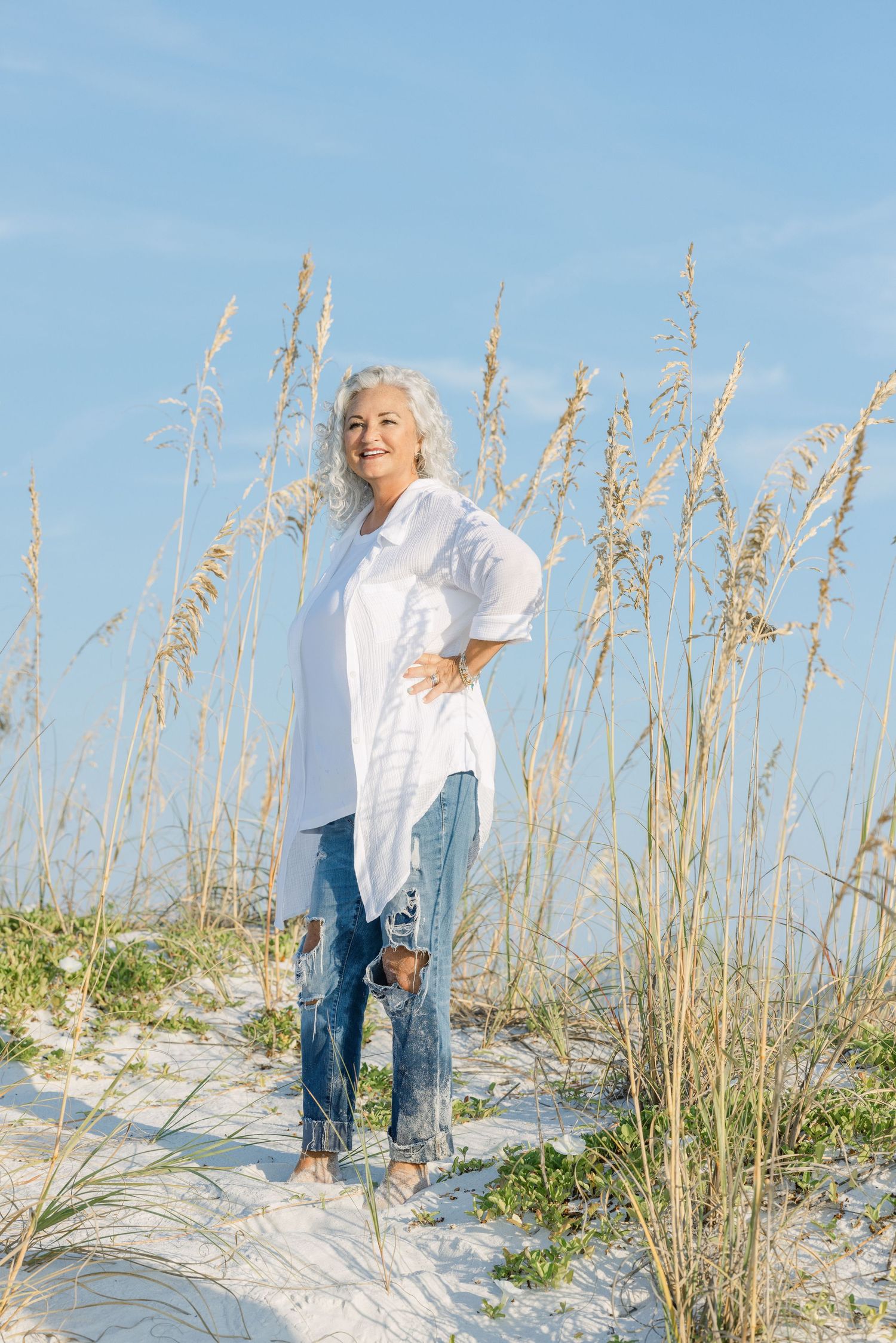 Sea oats sway in the breeze against white sand dunes and blue sky at a peaceful coastal beach setting.
