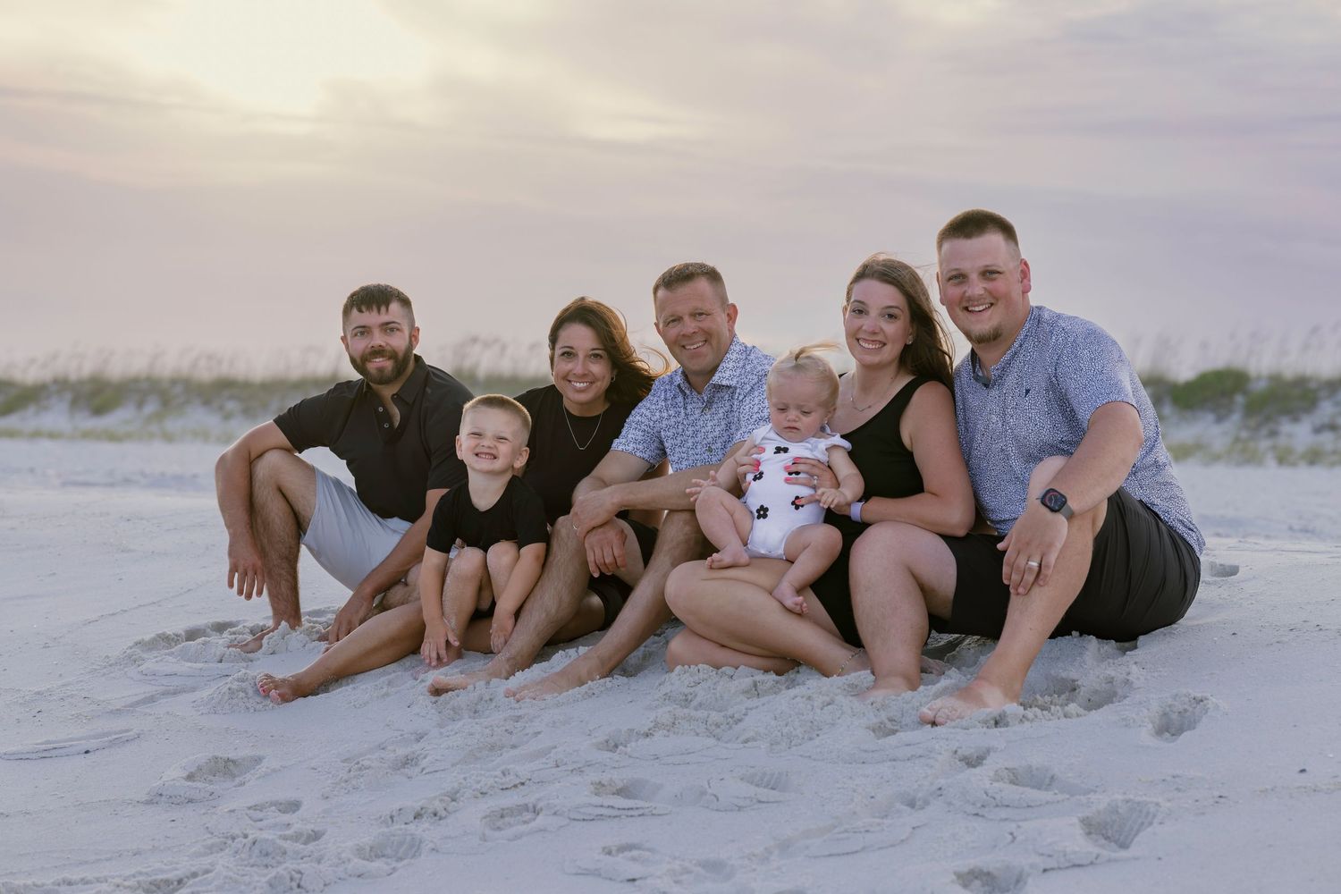 Family group portrait sitting on sandy beach at sunset with sea oats behind them.