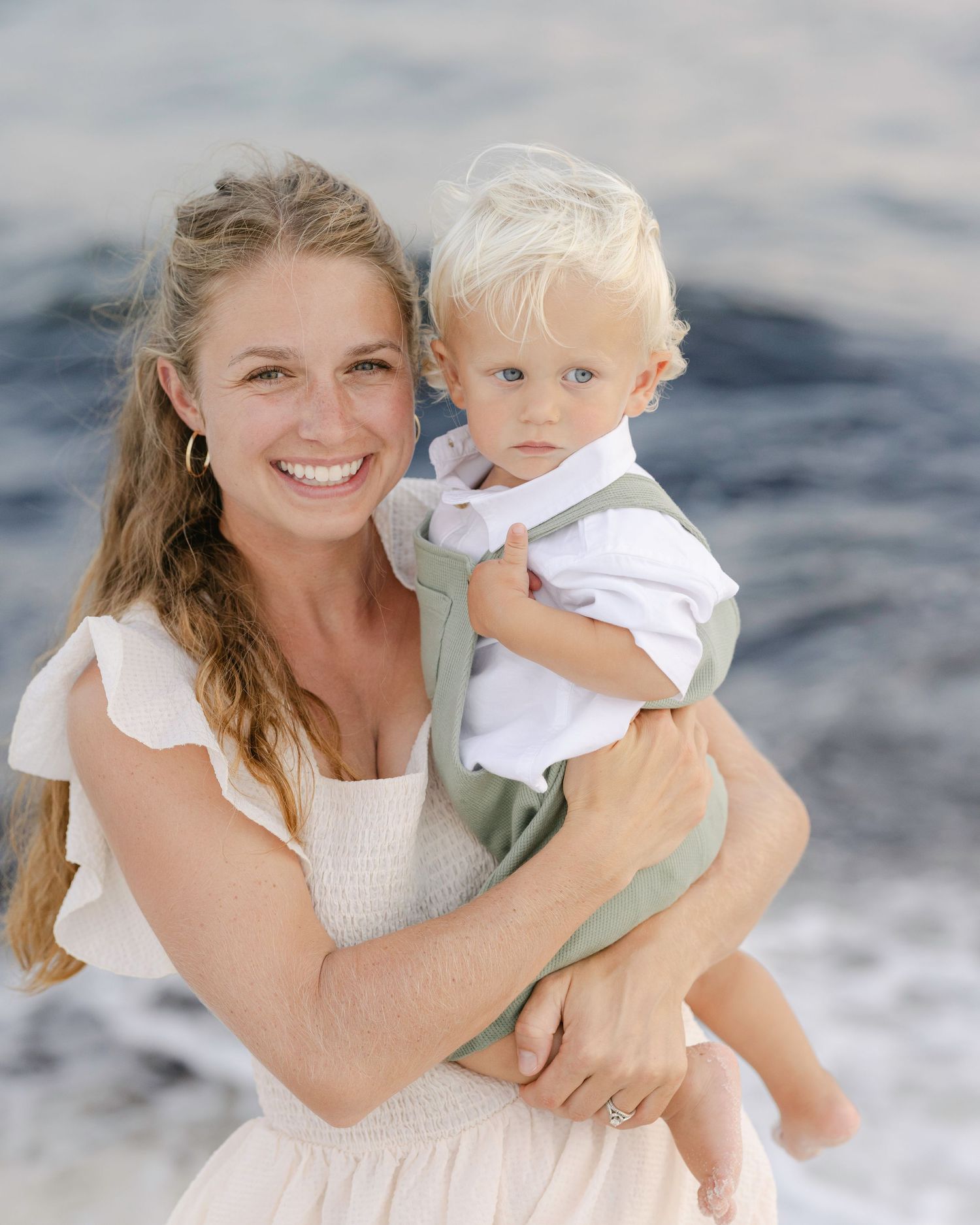A peaceful beach scene with ocean waves in the background and soft natural lighting framing the tender family moment.