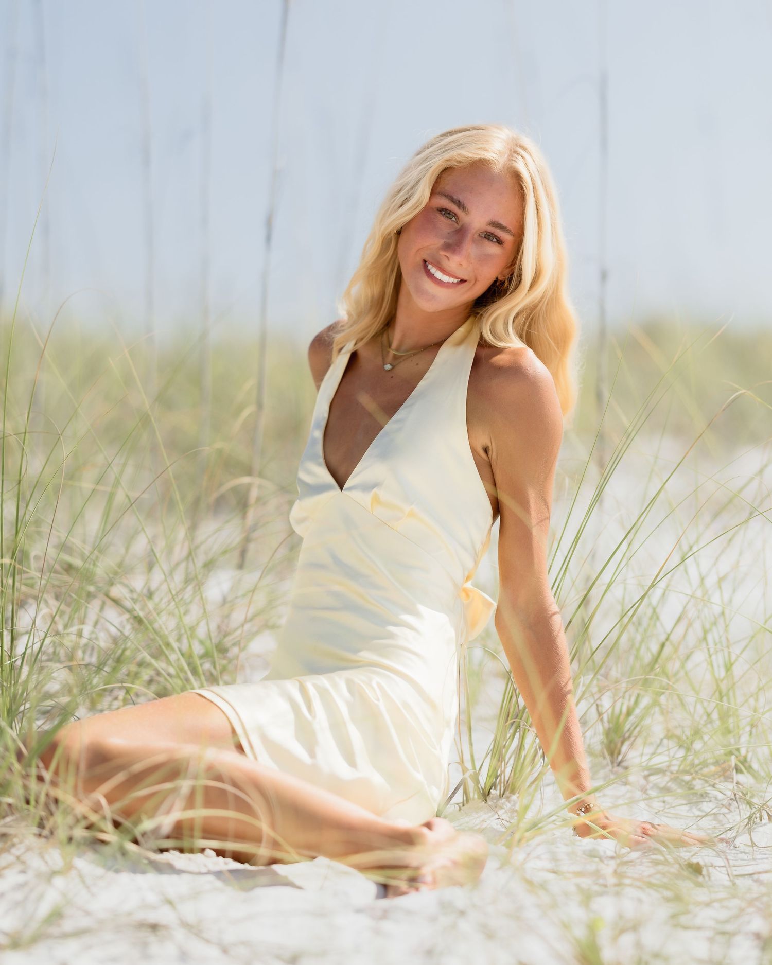 Blonde woman in cream dress sitting on beach sand dunes.