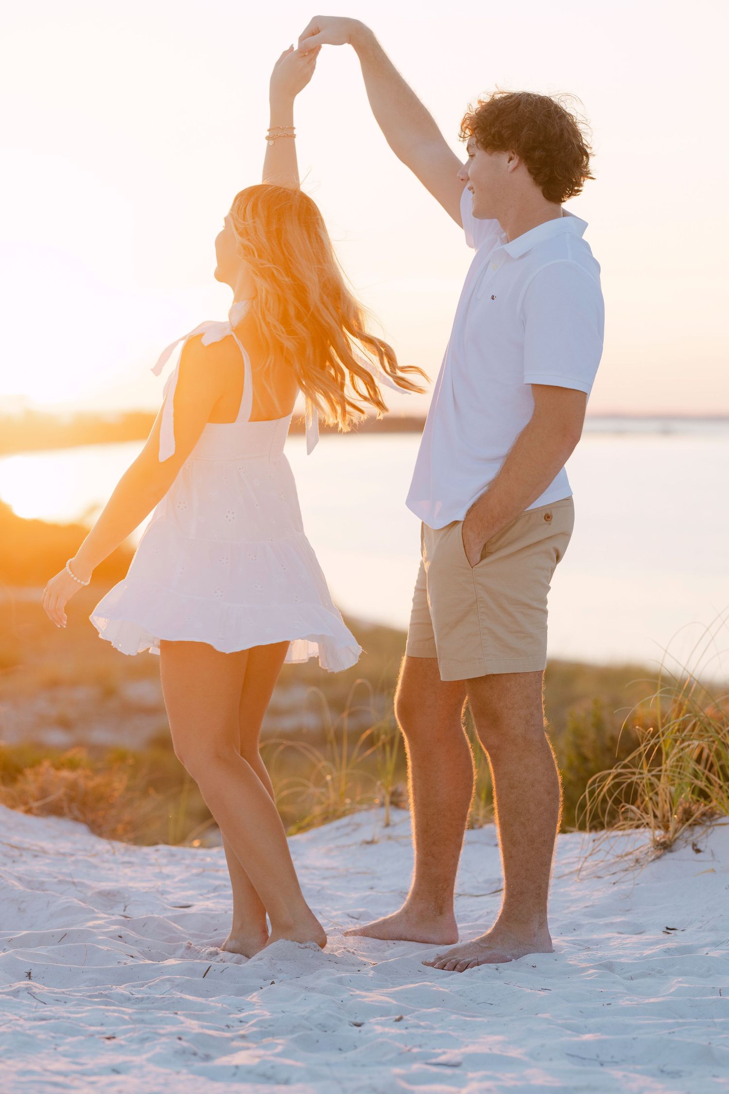 Couple standing together on sandy beach during golden sunset with feet in soft white sand.