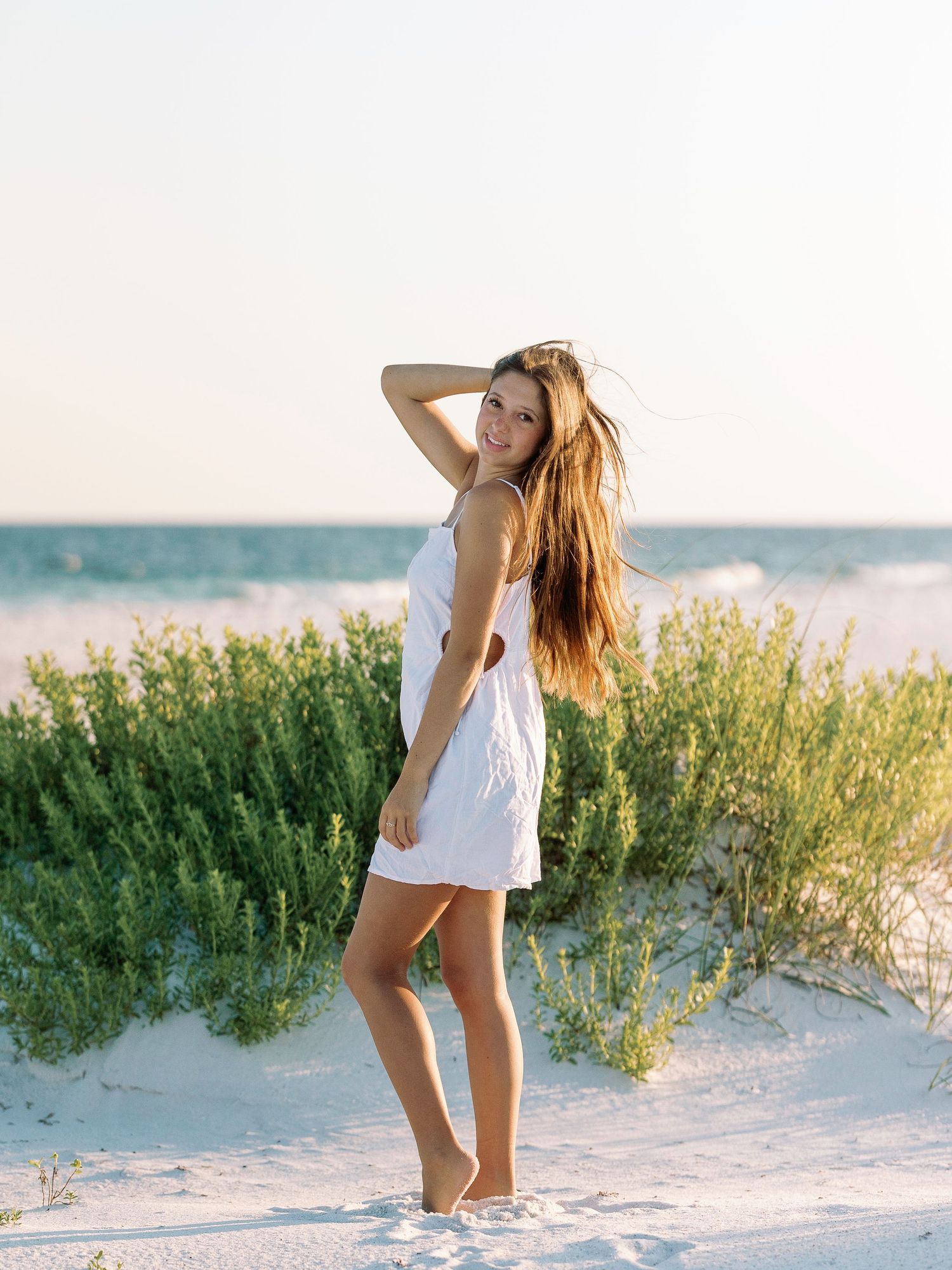 Five connected photographs show a woman in a white dress posing gracefully among beach dunes at sunset.