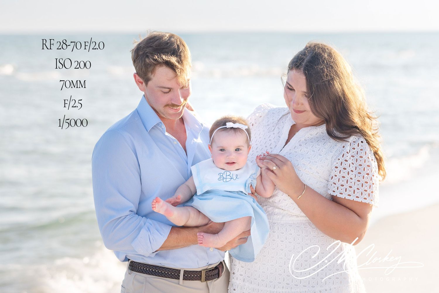 A family in soft colored clothing poses together at the beach during a sunset photoshoot by the ocean.