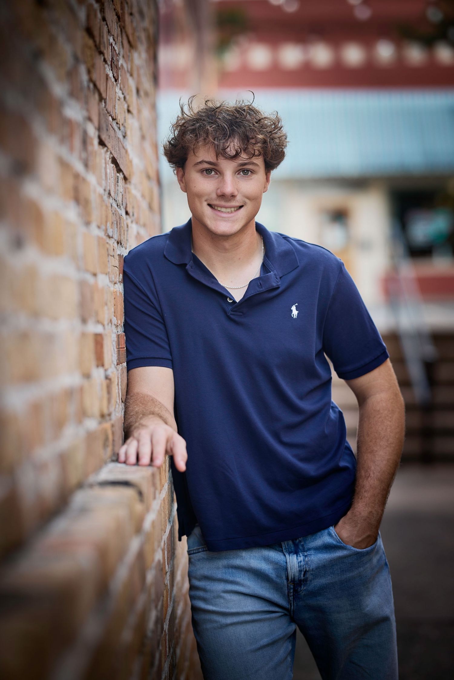 Smiling teen in navy Ralph Lauren polo leans against brick wall outdoors.