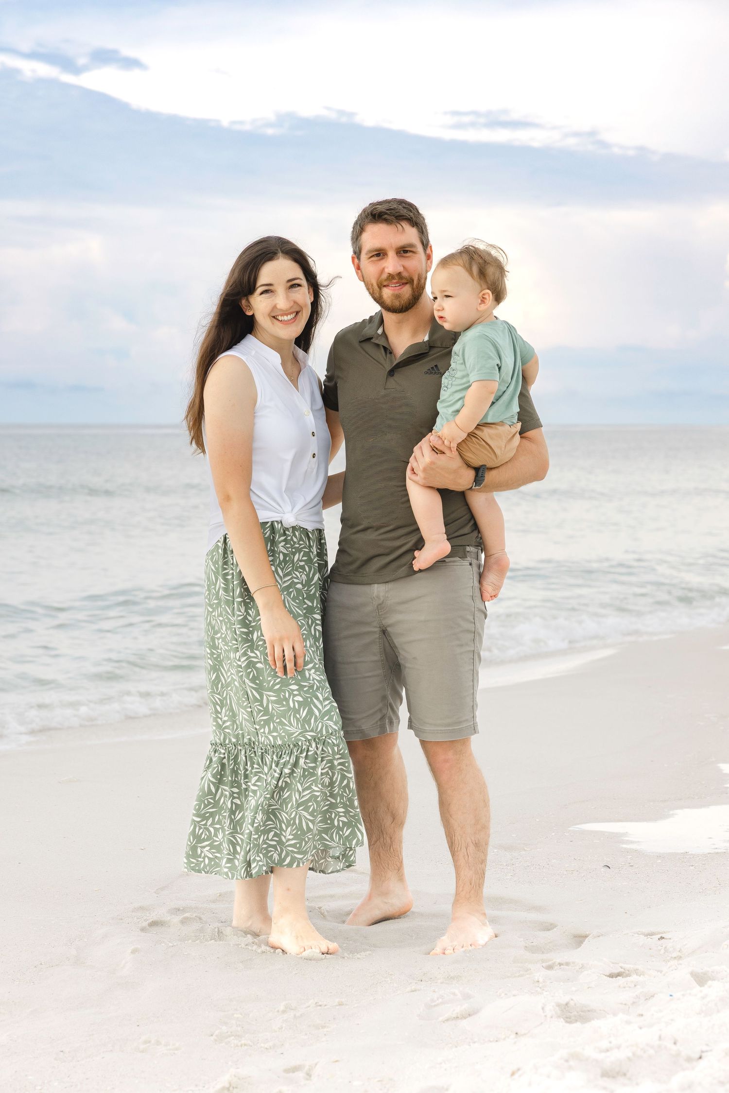 Family enjoying a beach photo session together on white sand with cloudy sky in the background.