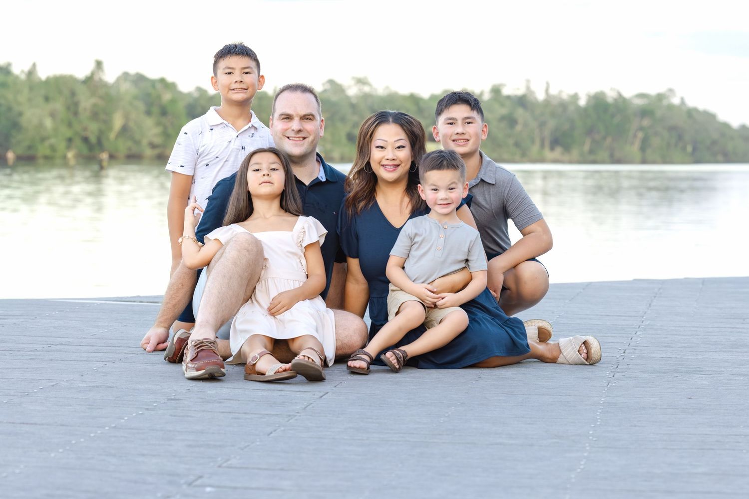 Happy family of six posing together outdoors near a lake, smiling for a portrait on a sunny day.