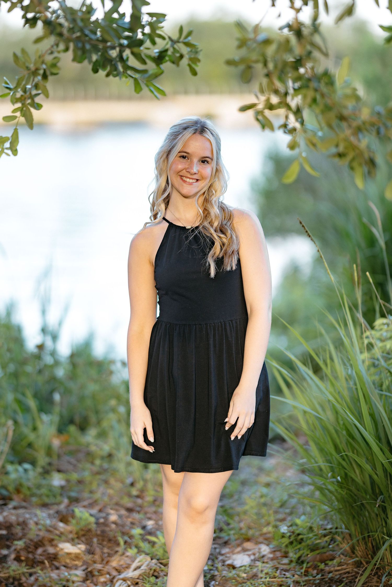 Natural light portrait featuring a black dress against lush greenery and water backdrop.