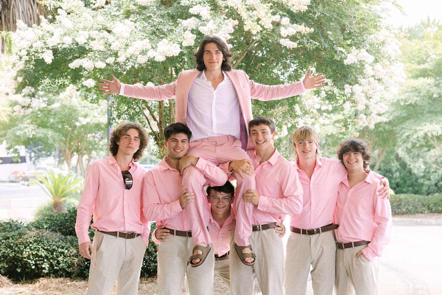 Wedding party wearing coordinated pink and khaki outfits standing together outdoors.